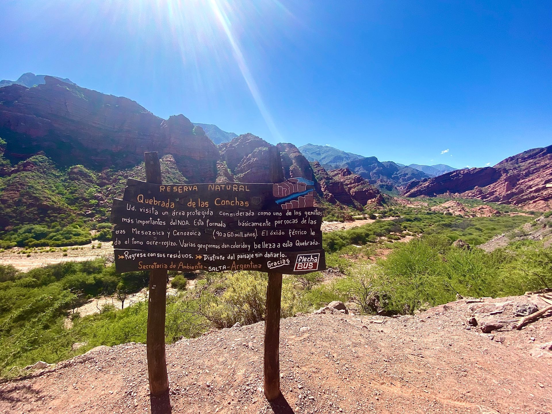 A wooden sign in the middle of a desert with mountains in the background.