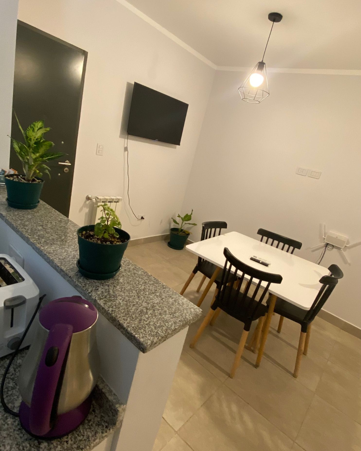 A dining room with a table and chairs and a tv on the wall