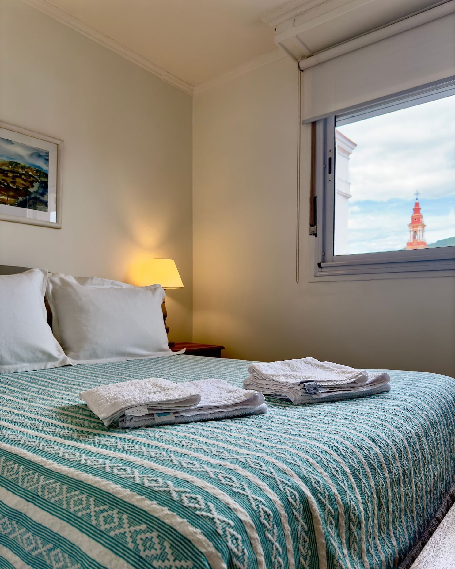 A bedroom with a bed and a window with a clock tower in the background.