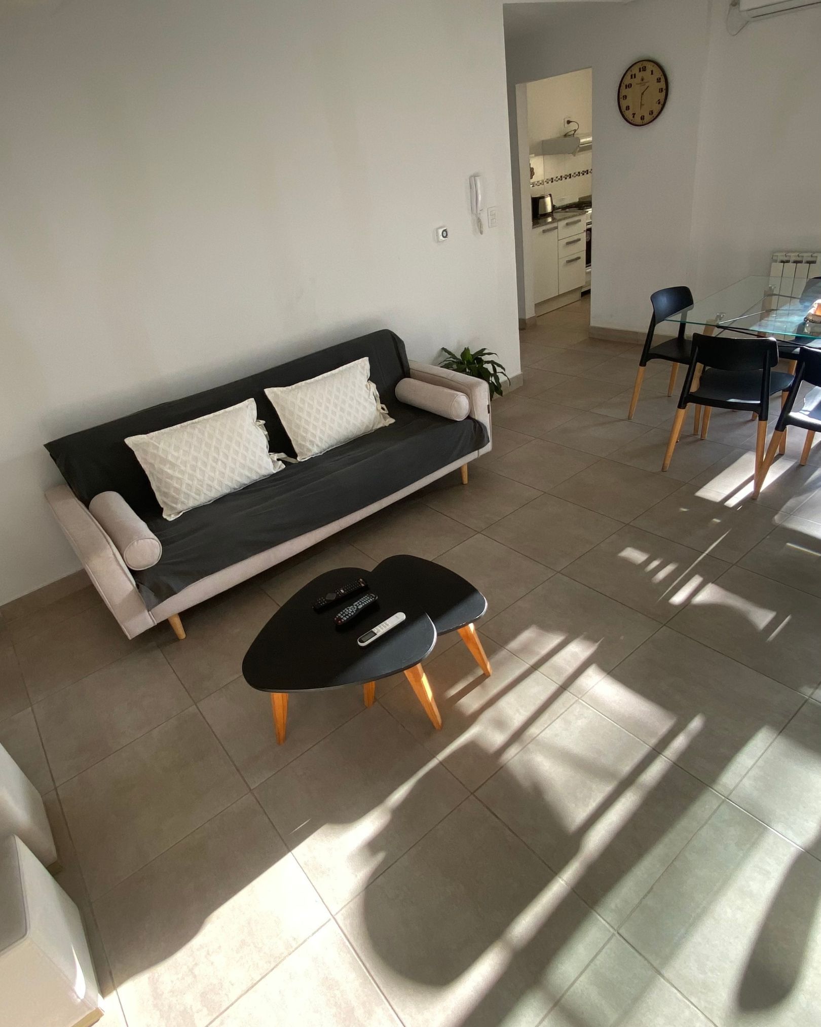 A living room with a couch , table , chairs and a clock on the wall.