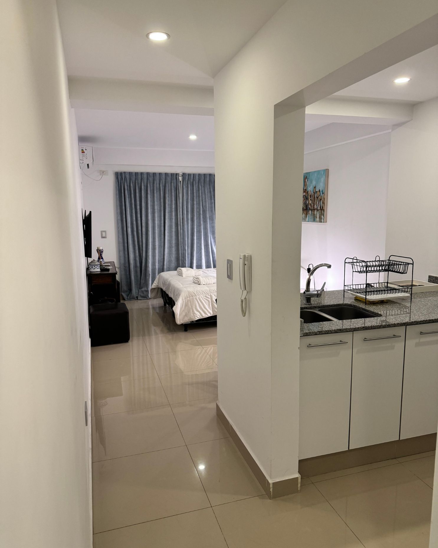 A hallway leading to a bedroom with a bed and a kitchen.