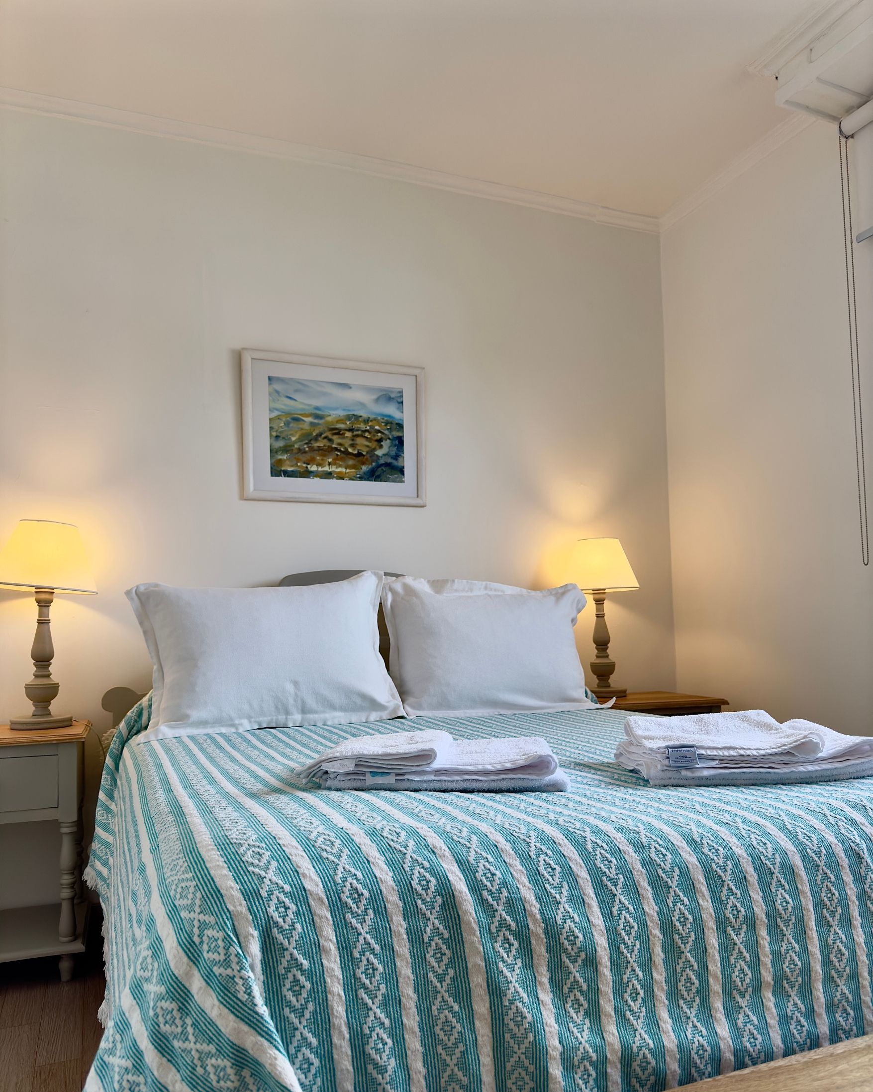 A bedroom with a bed , two lamps and a painting on the wall.
