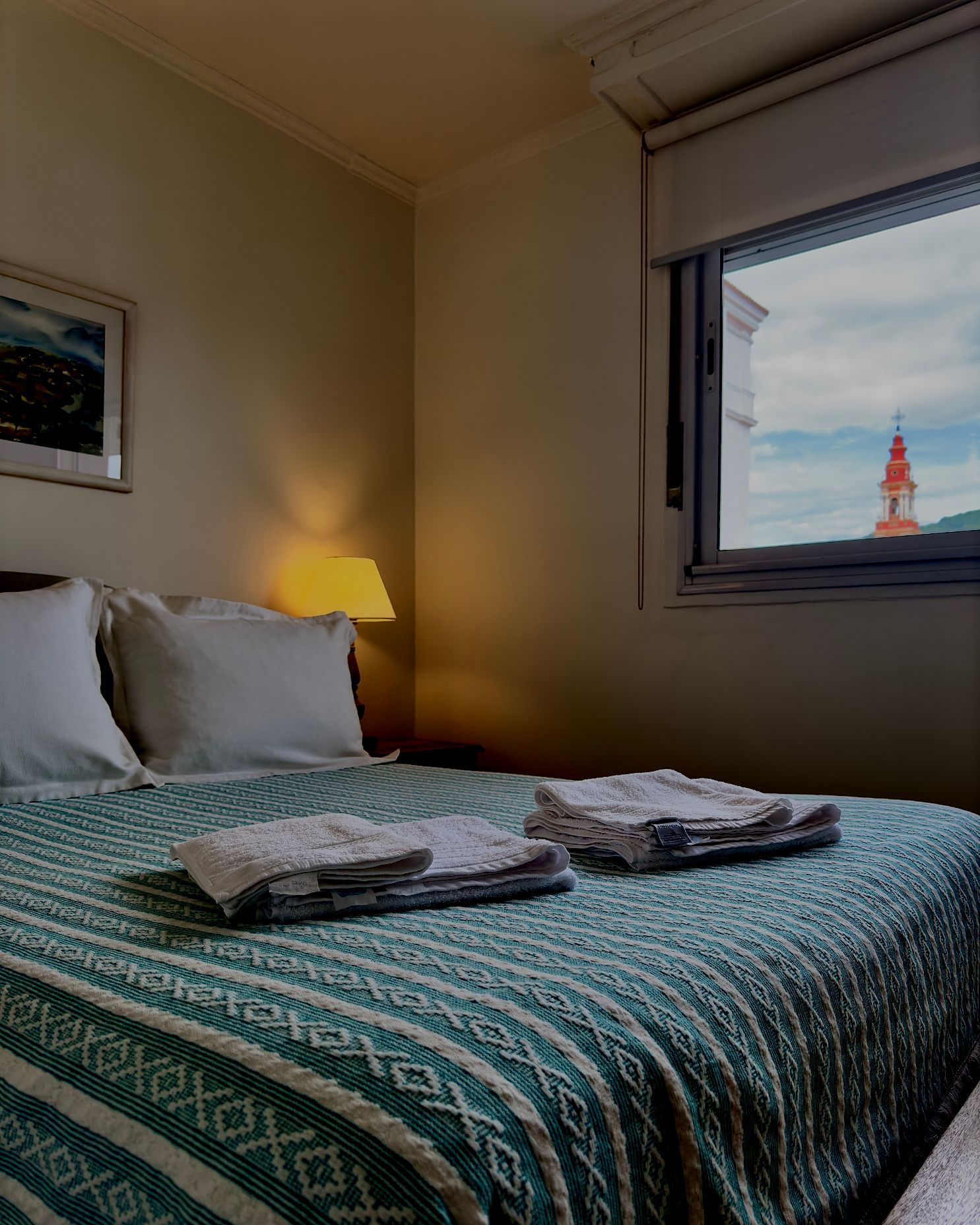 A bedroom with a bed and a window with a clock tower in the background.