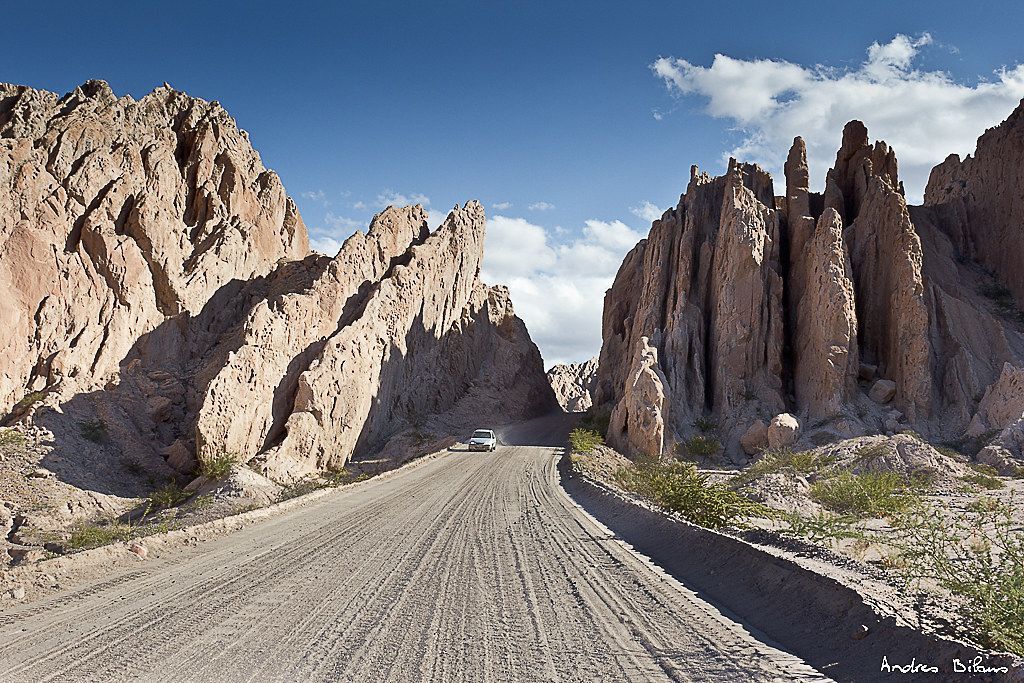 A car is driving down a dirt road in the desert