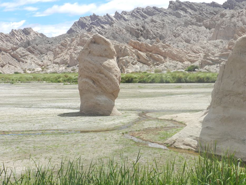 A large rock in the middle of a desert with mountains in the background