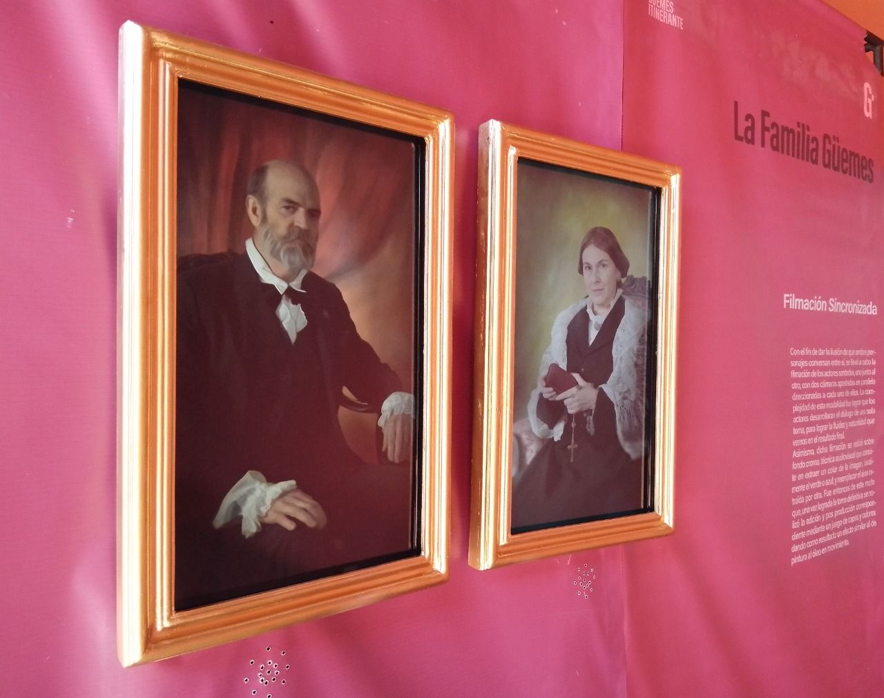 Two framed portraits of a man and a woman are hanging on a pink wall.