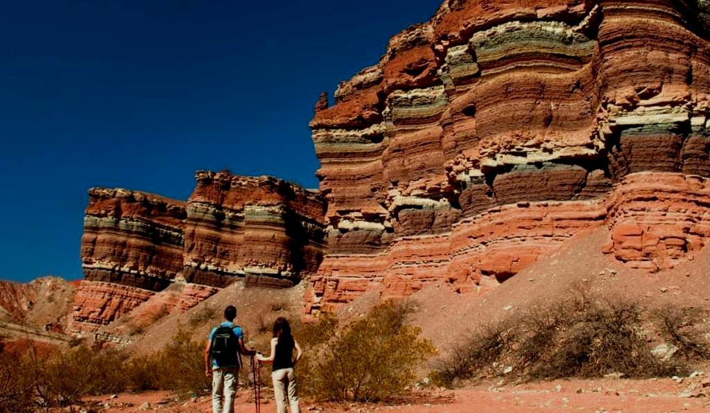 A man and a woman are standing in front of a rock formation.