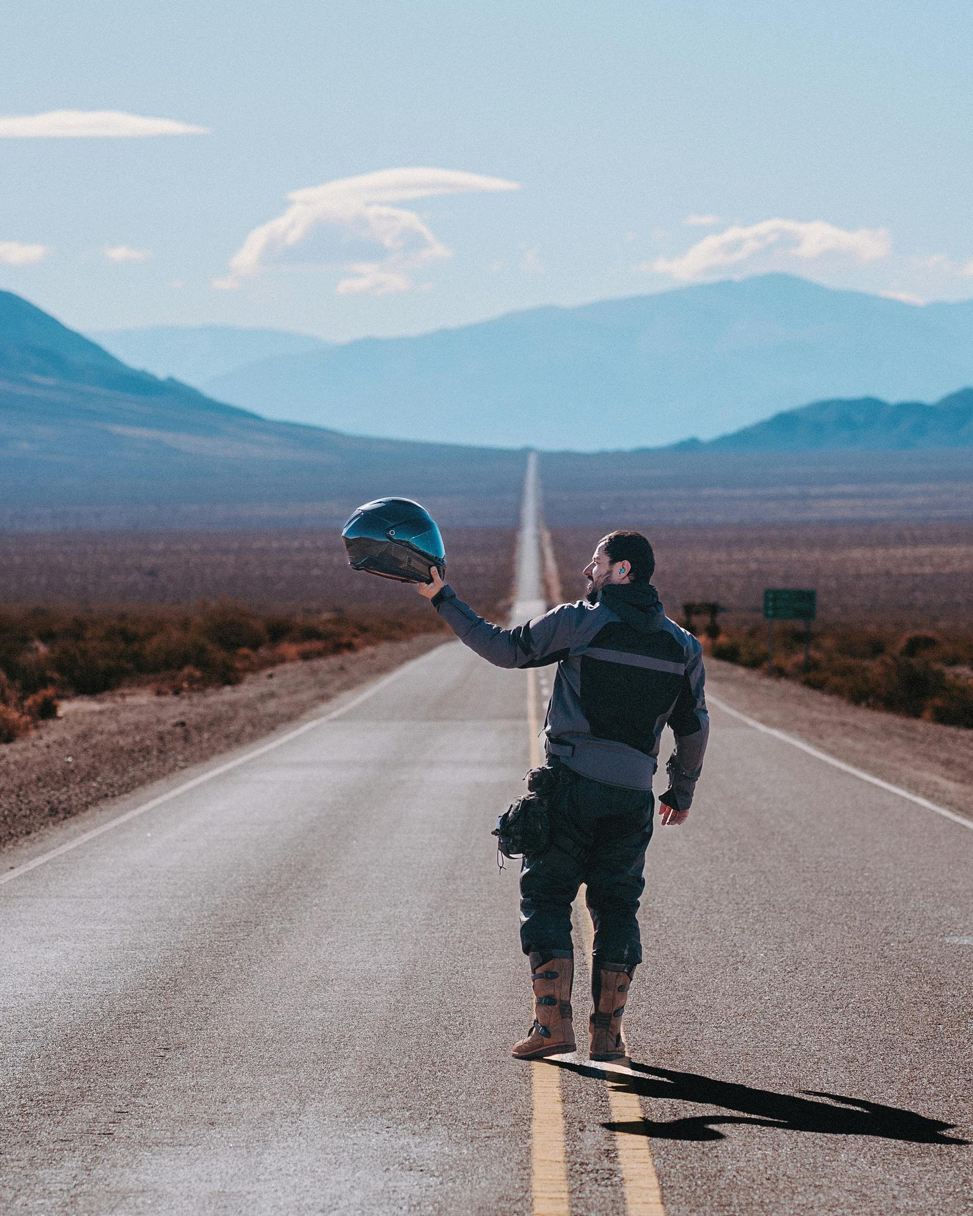 A man standing on the side of a road holding a helmet
