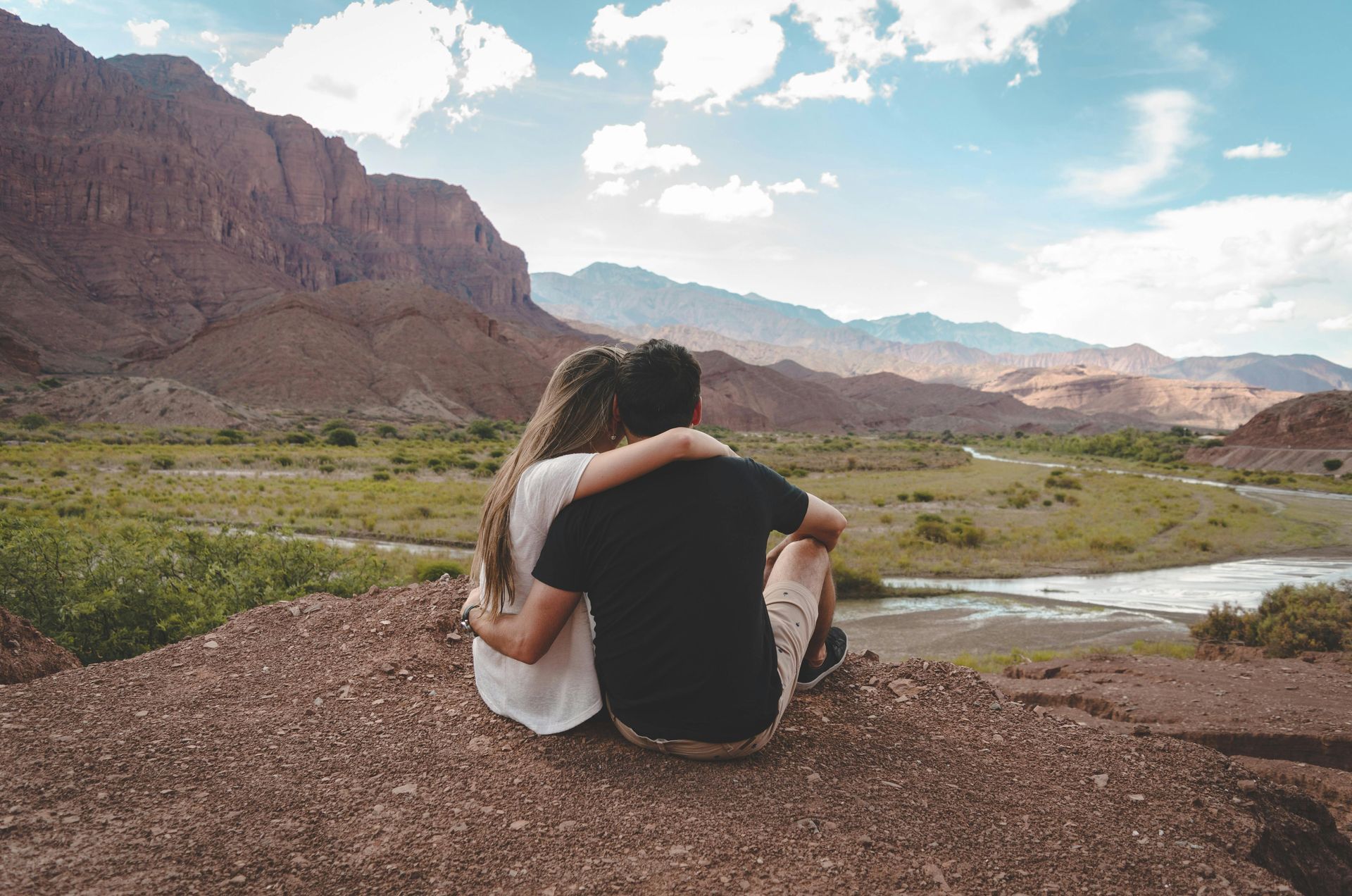 A man and a woman are sitting on top of a rock looking at the mountains.