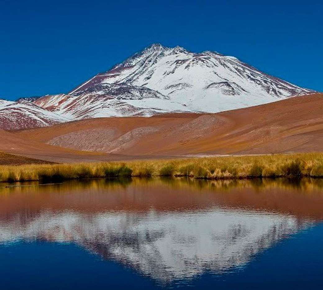 A mountain covered in snow is reflected in a lake.