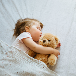 a little girl is sleeping with a teddy bear