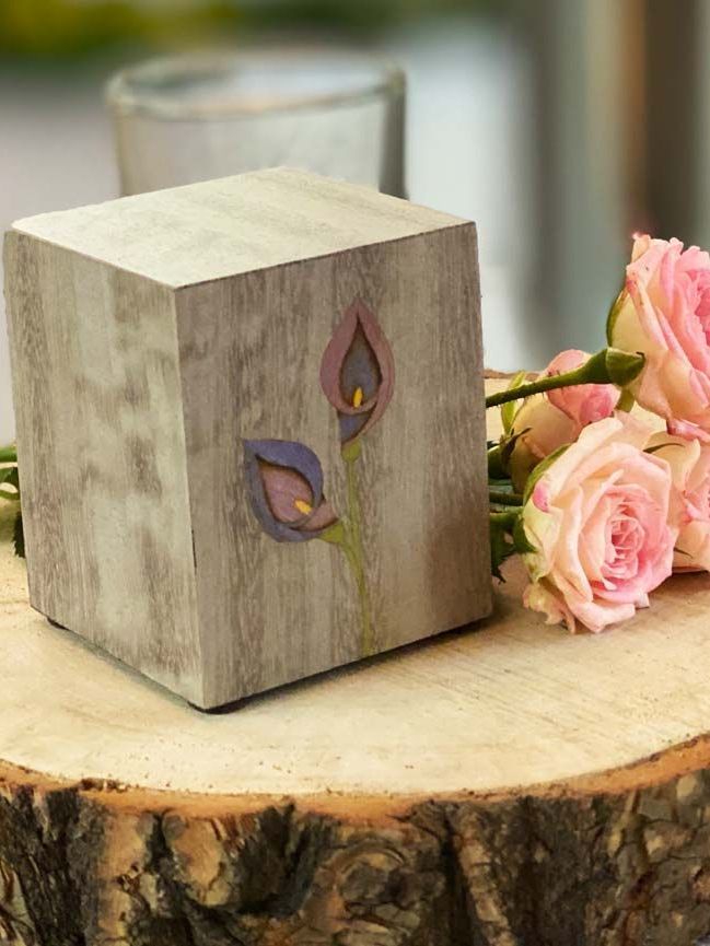 Holzurne in Form eines Würfels auf Holzstamm mit rosa Rosen