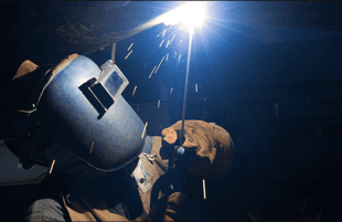 A man in a welding mask burning steel