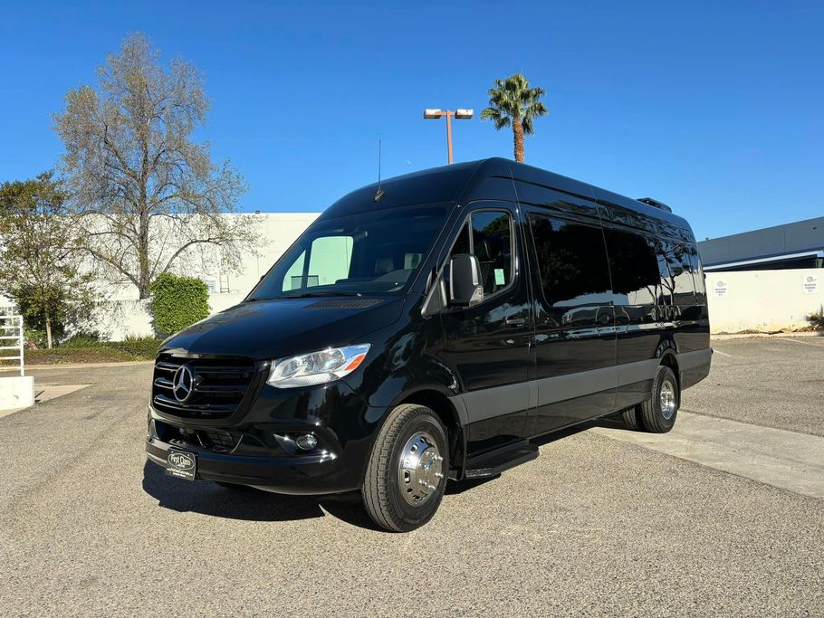 A black van is parked in a gravel lot in front of a building.