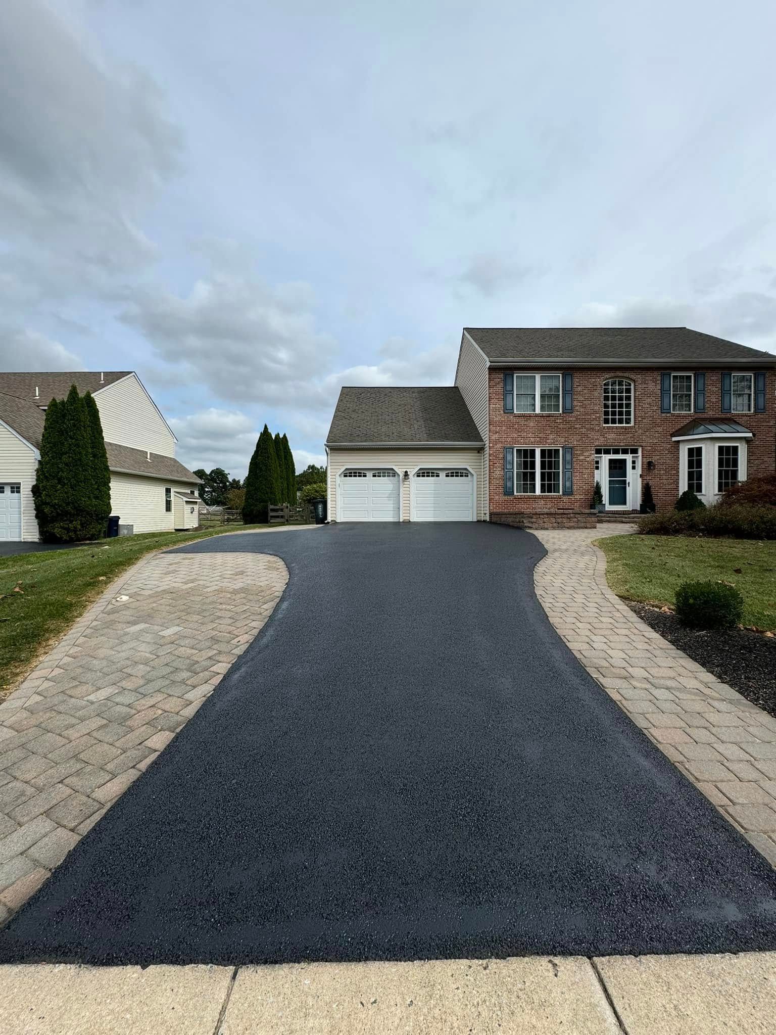 A brick house with a black driveway leading to it.