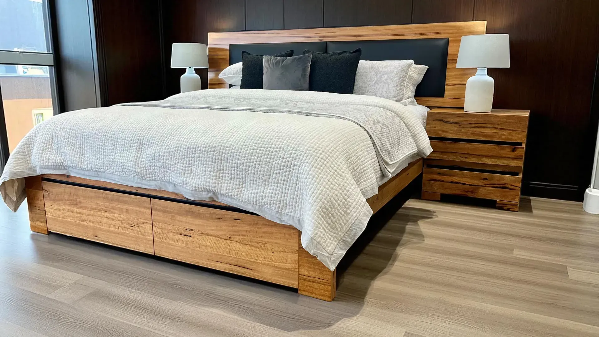 Wooden bed with built-in drawers, nightstand, and lamps; bed has light-colored bedding and pillows.