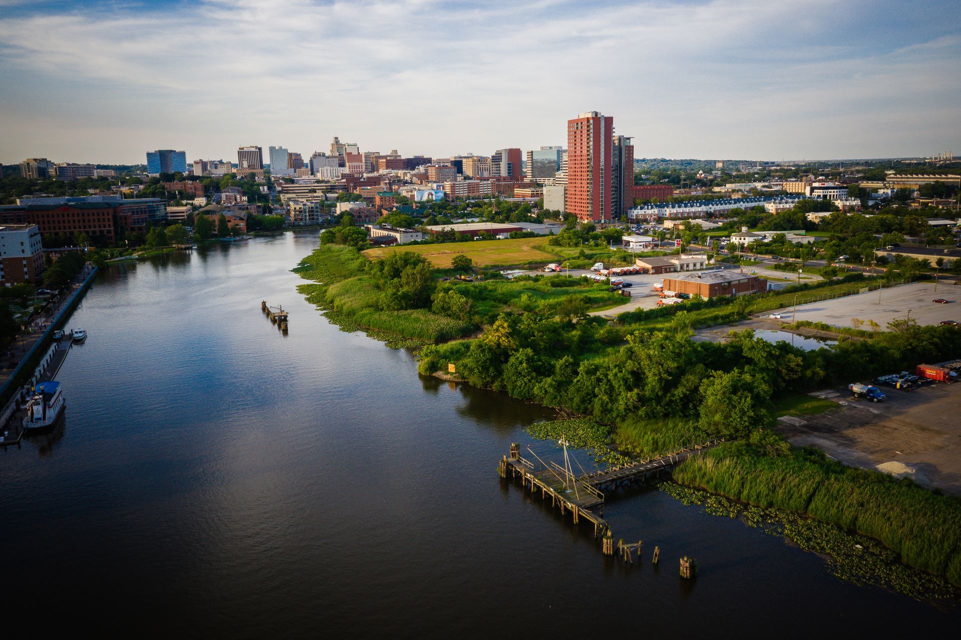 Aerial view of a river winding through a city skyline with green banks and buildings at sunset