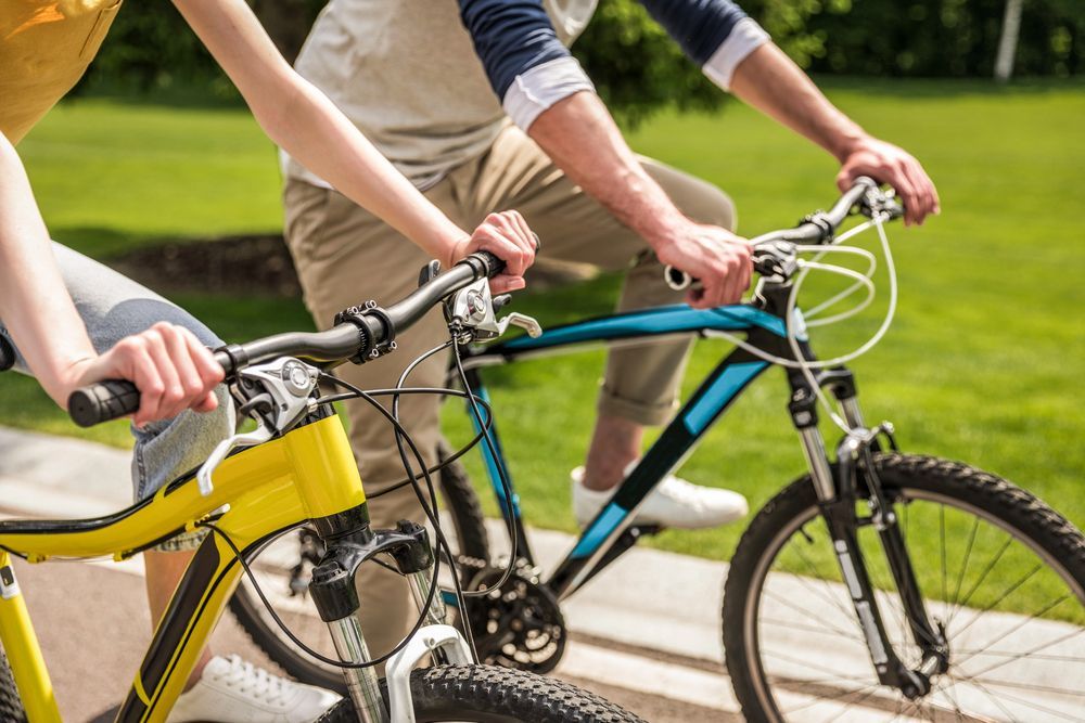 Due persone vanno in bicicletta su un sentiero asfaltato, in una giornata di sole. Biciclette gialle e blu.