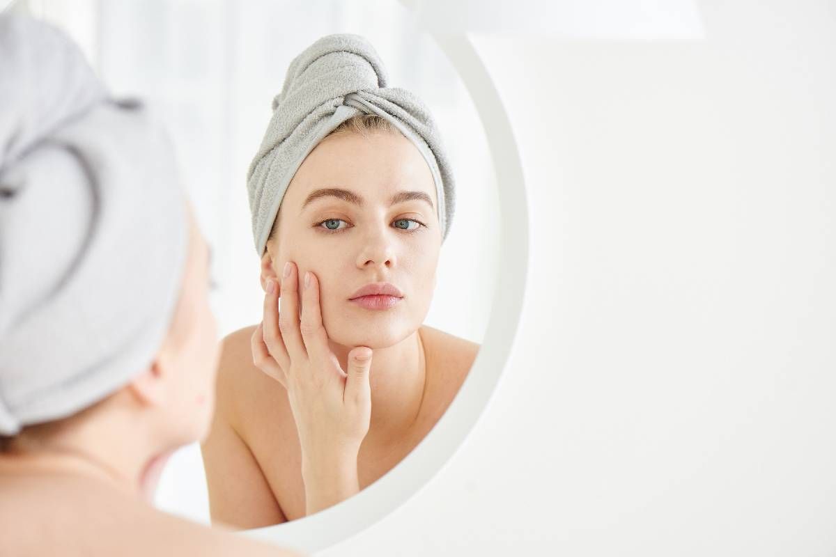 Woman with towel on head looks and touches her face in the mirror after acne treatment near Lexington, Kentucky (KY)