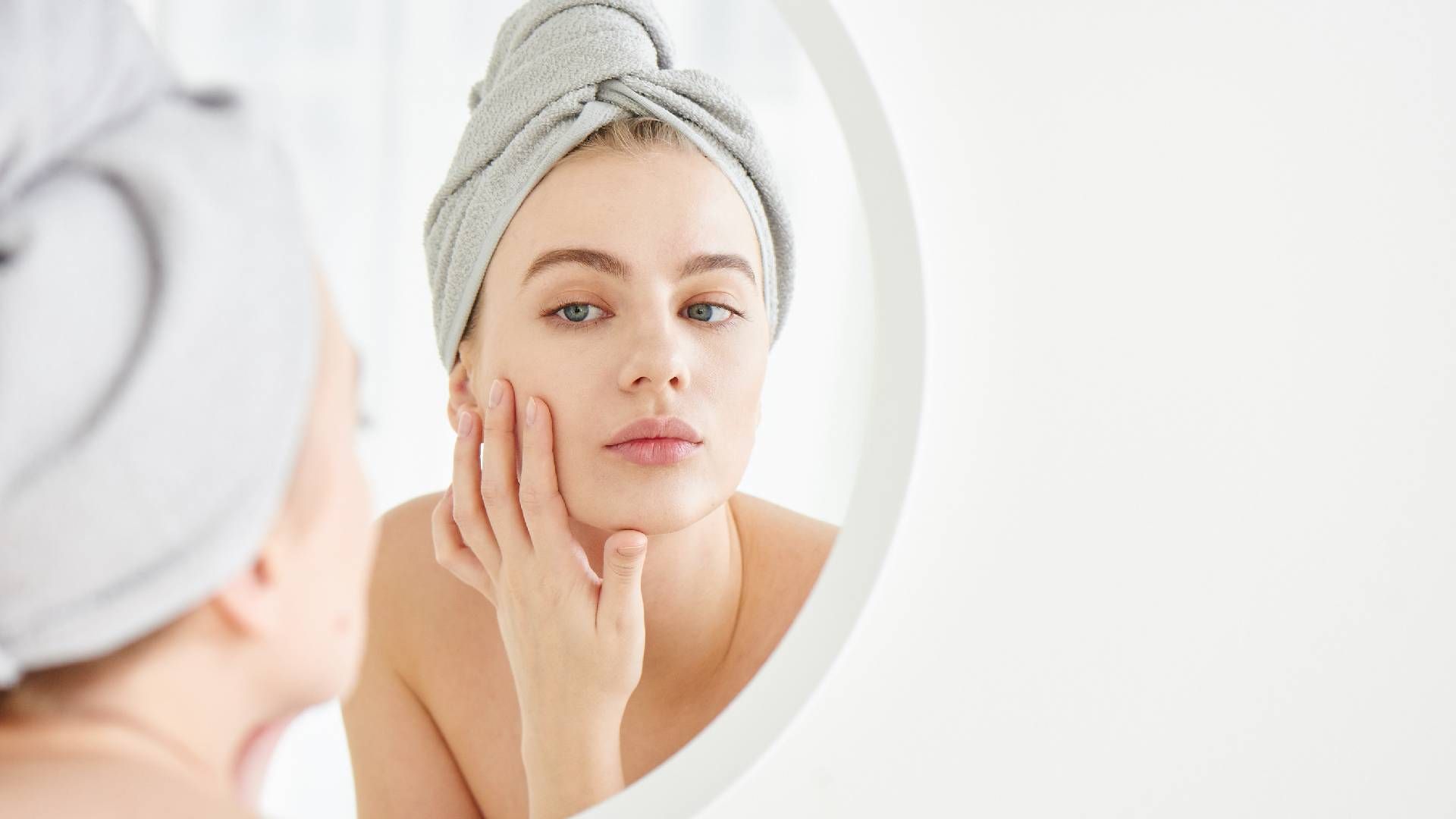 Woman with towel on head looks and touches her face in the mirror after acne treatment near Lexingto