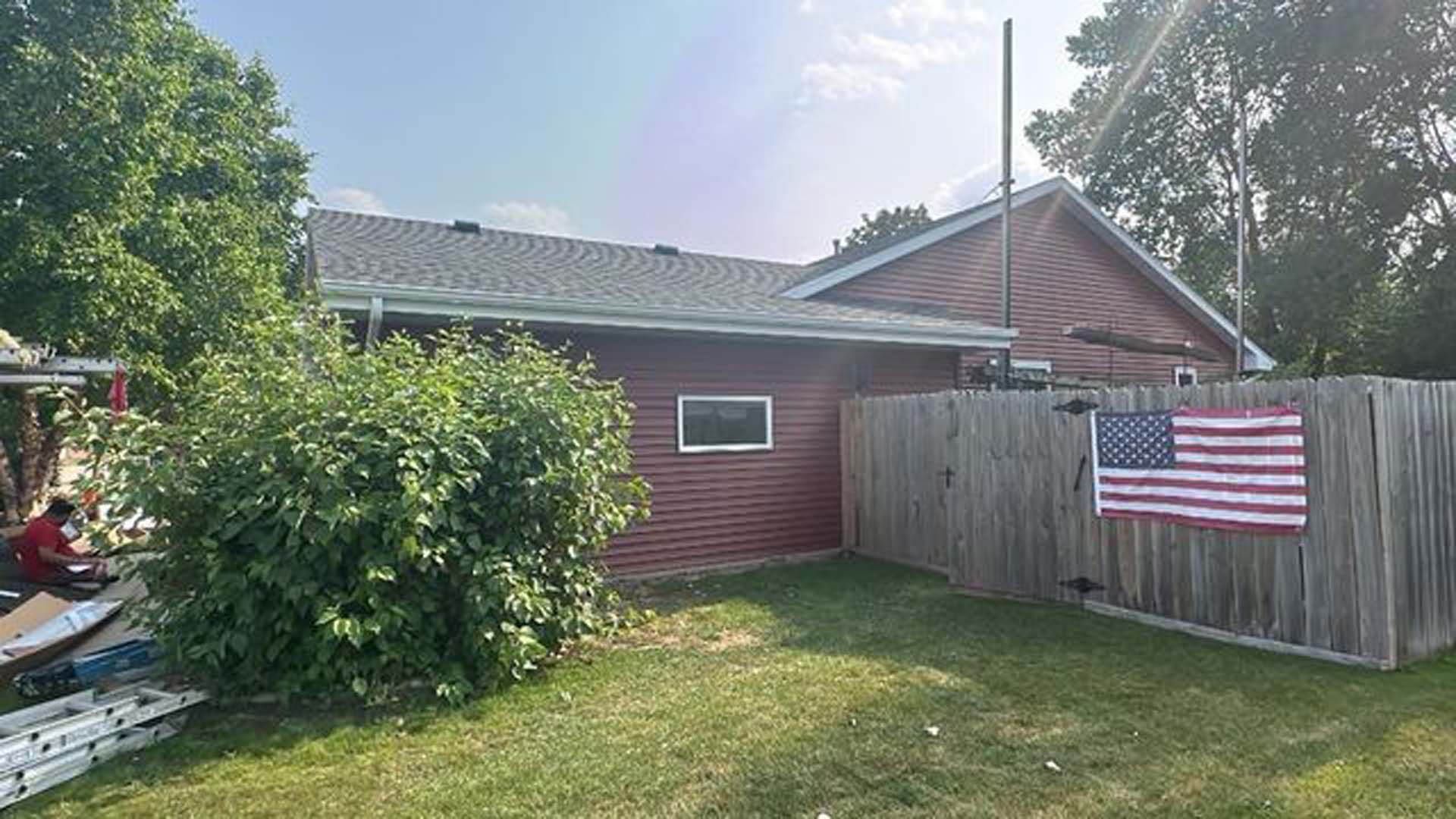 A red house with a wooden fence and an american flag in the backyard.
