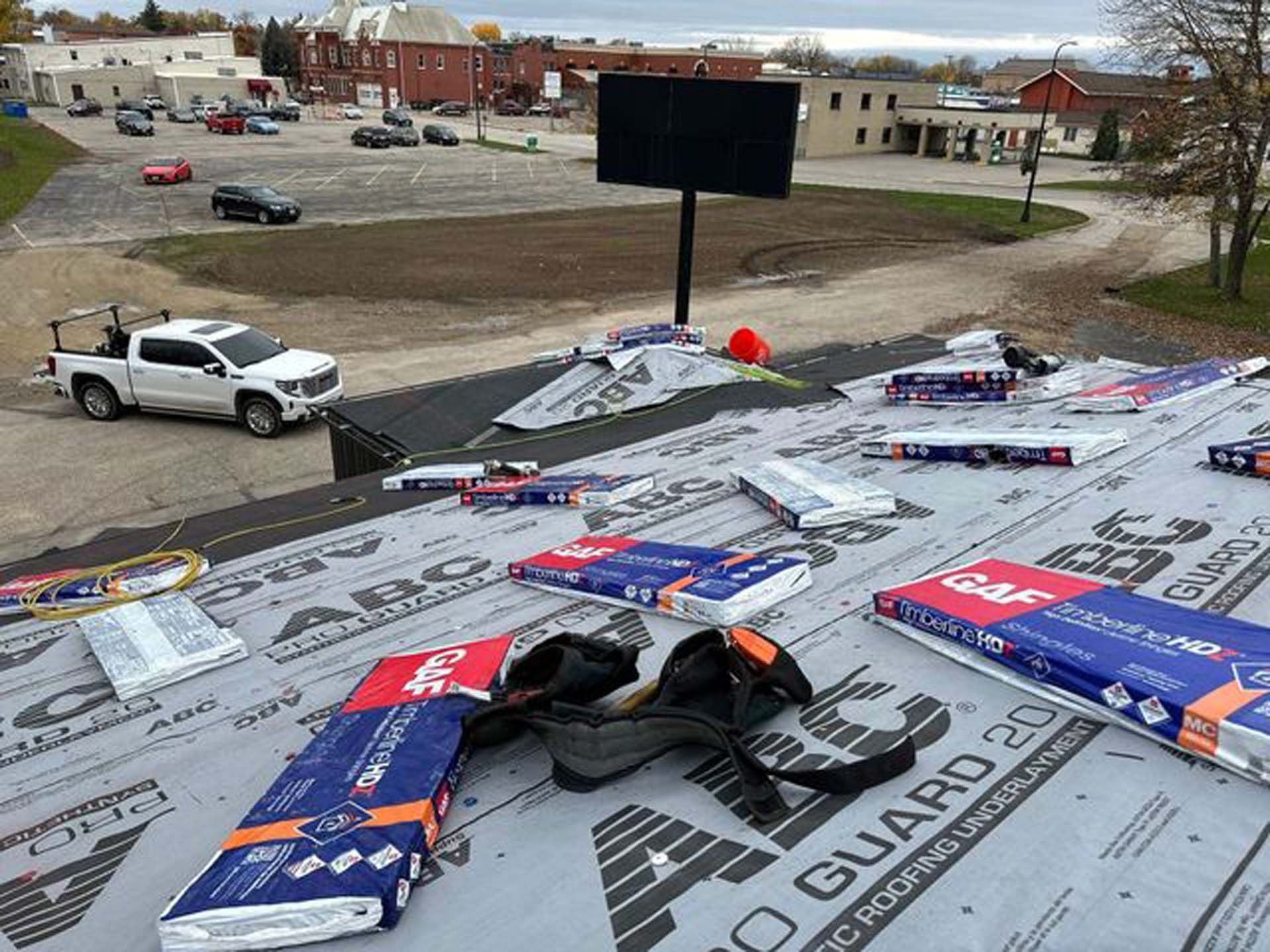 A white truck is parked on top of a roof covered in roofing materials.