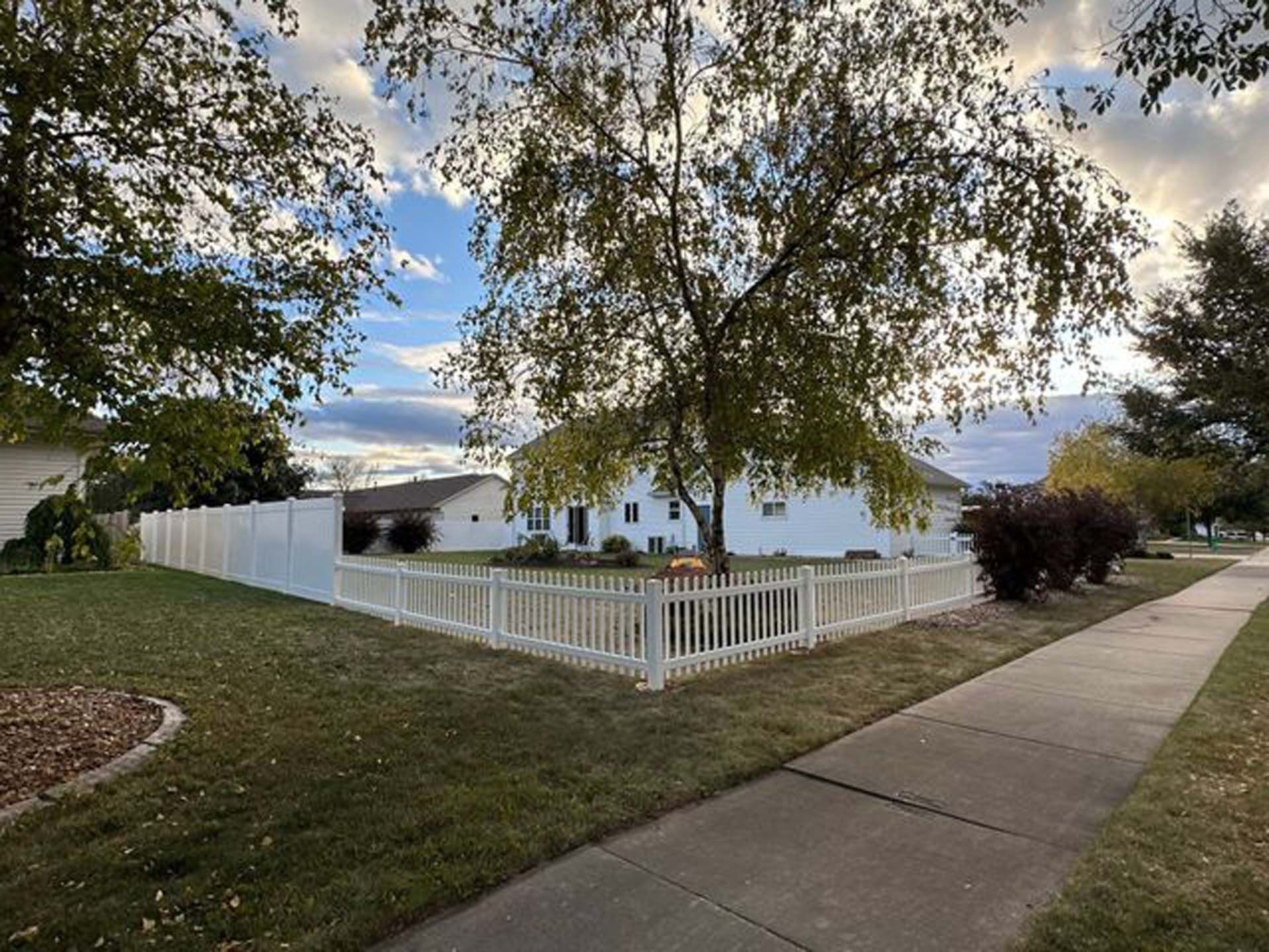 A white picket fence surrounds a yard in front of a house.