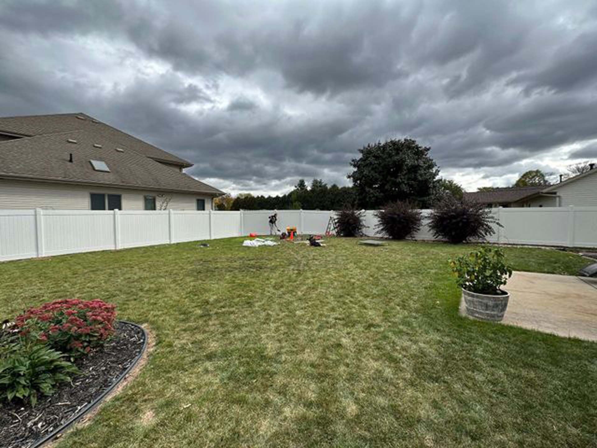 A backyard with a white fence and a house in the background.