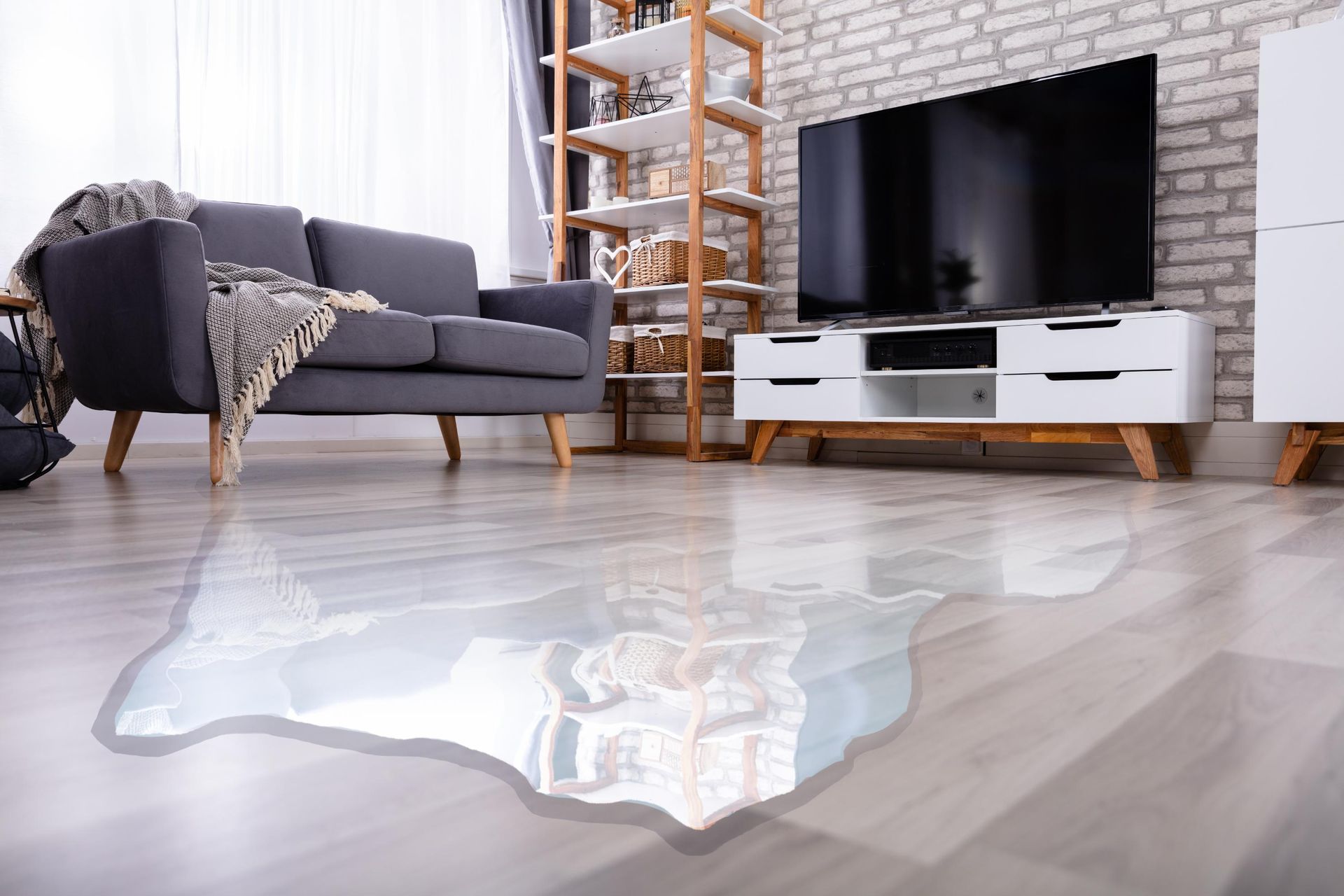 A living room with a couch, television, and a puddle of water on the floor.