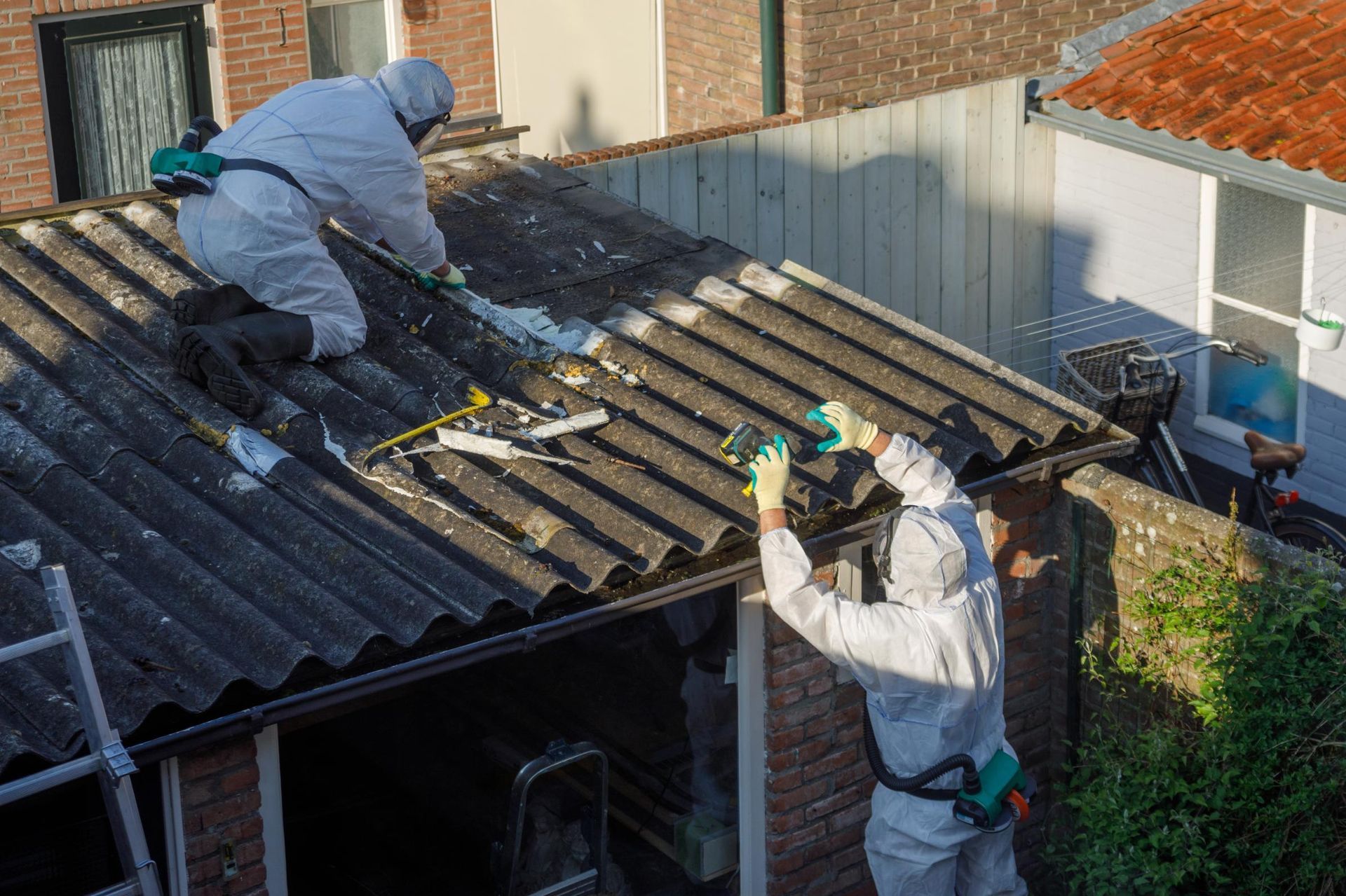 Two men in protective suits are working on the roof of a building.