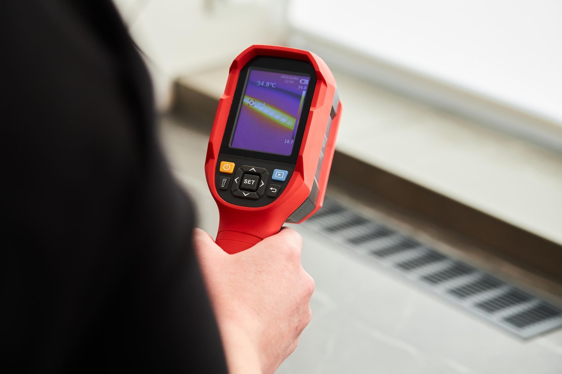 A person is holding a red thermal camera in their hand.