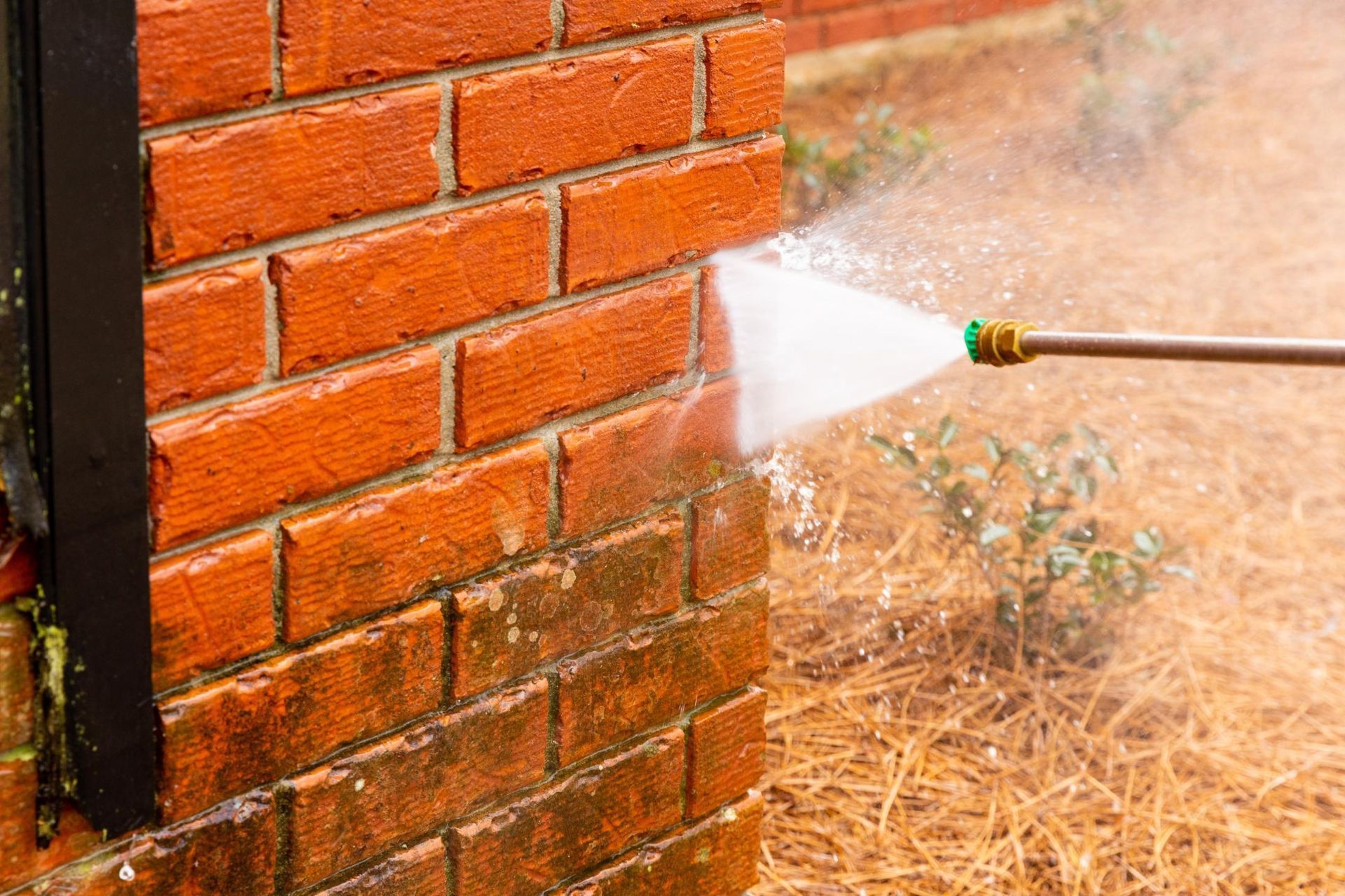 A person is cleaning a brick wall with a high pressure washer.