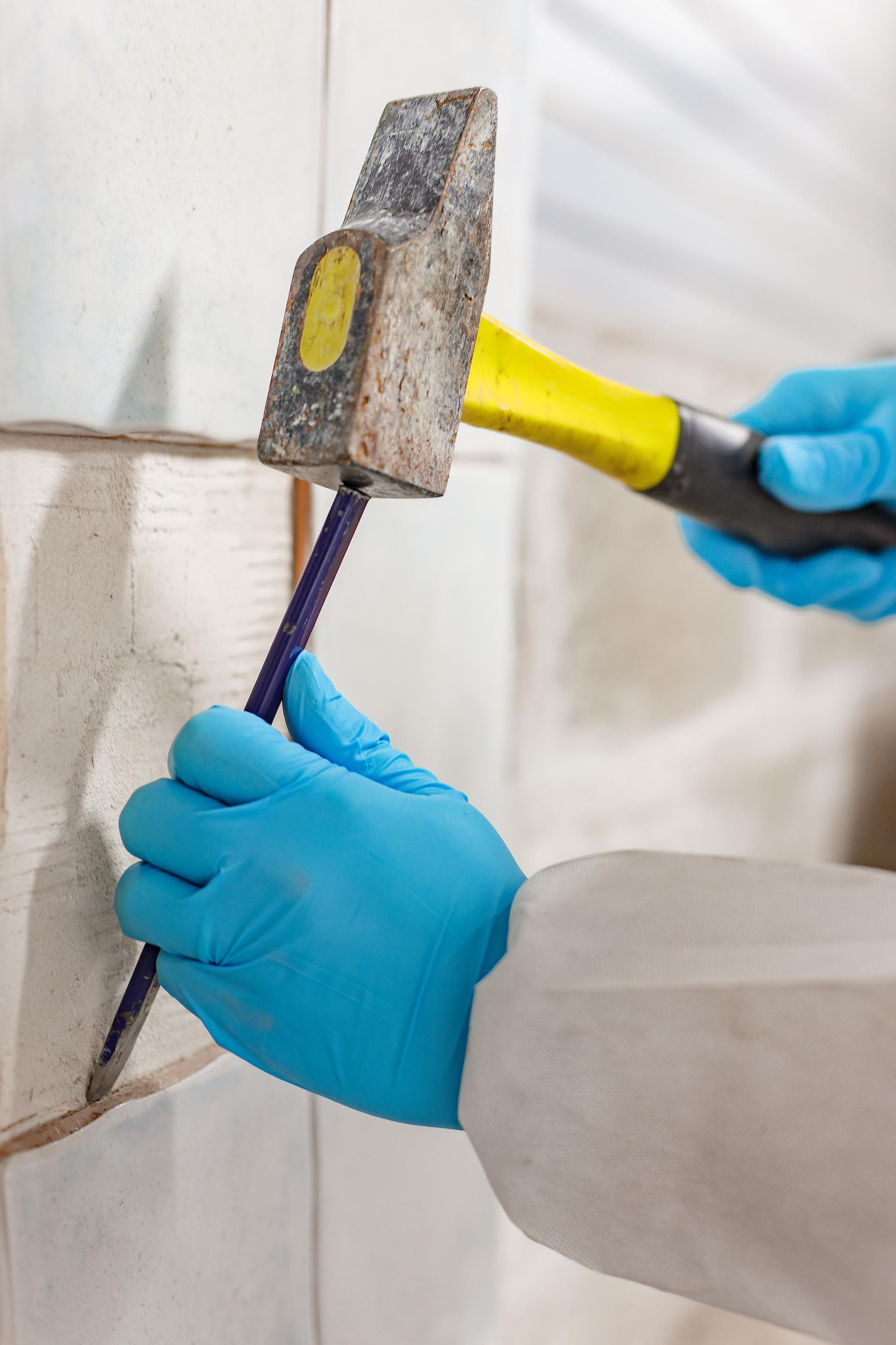 Asbestos surveyor taking a sample of building material with hammer and chisel.