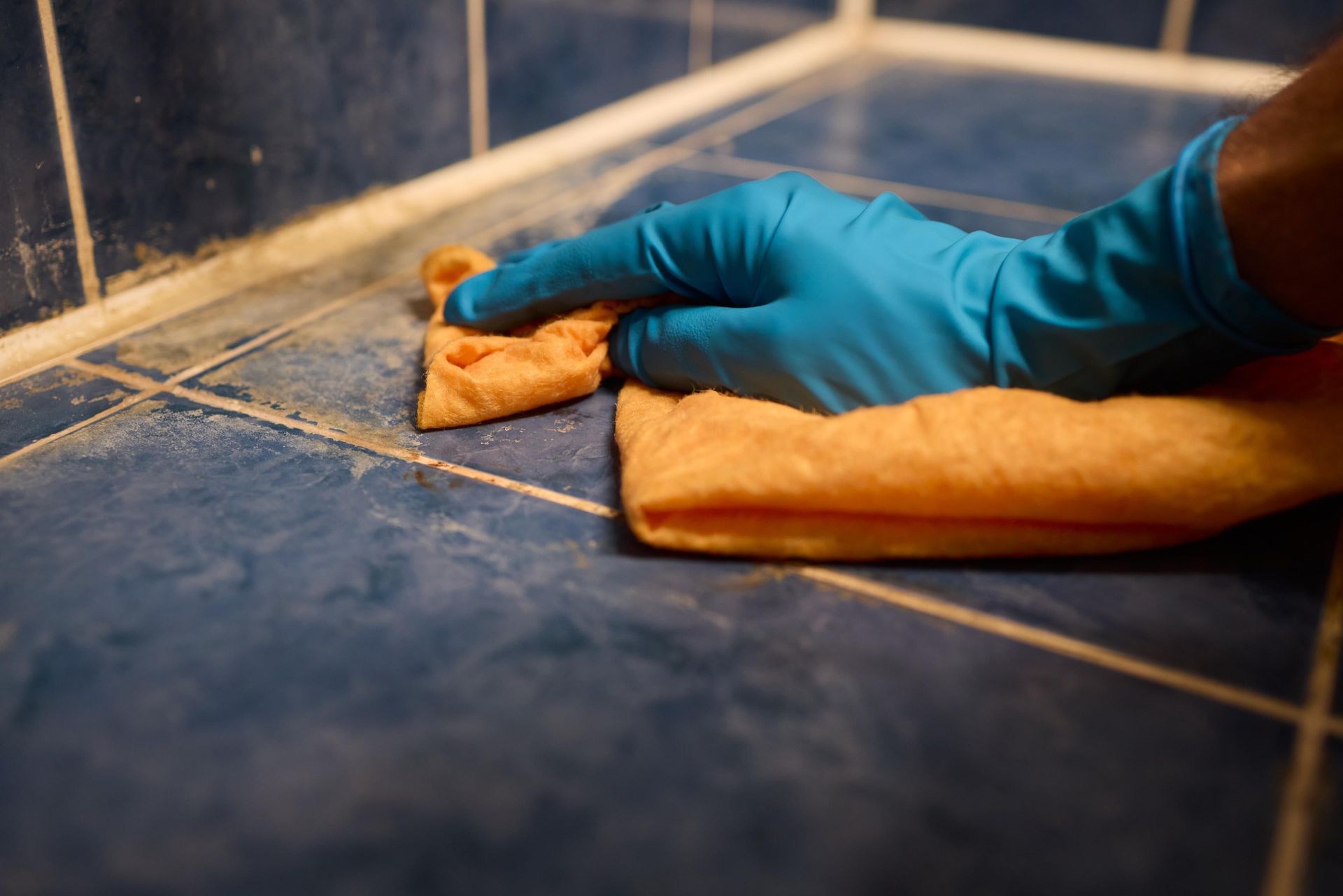 A person wearing blue gloves is cleaning a tiled floor with a cloth.