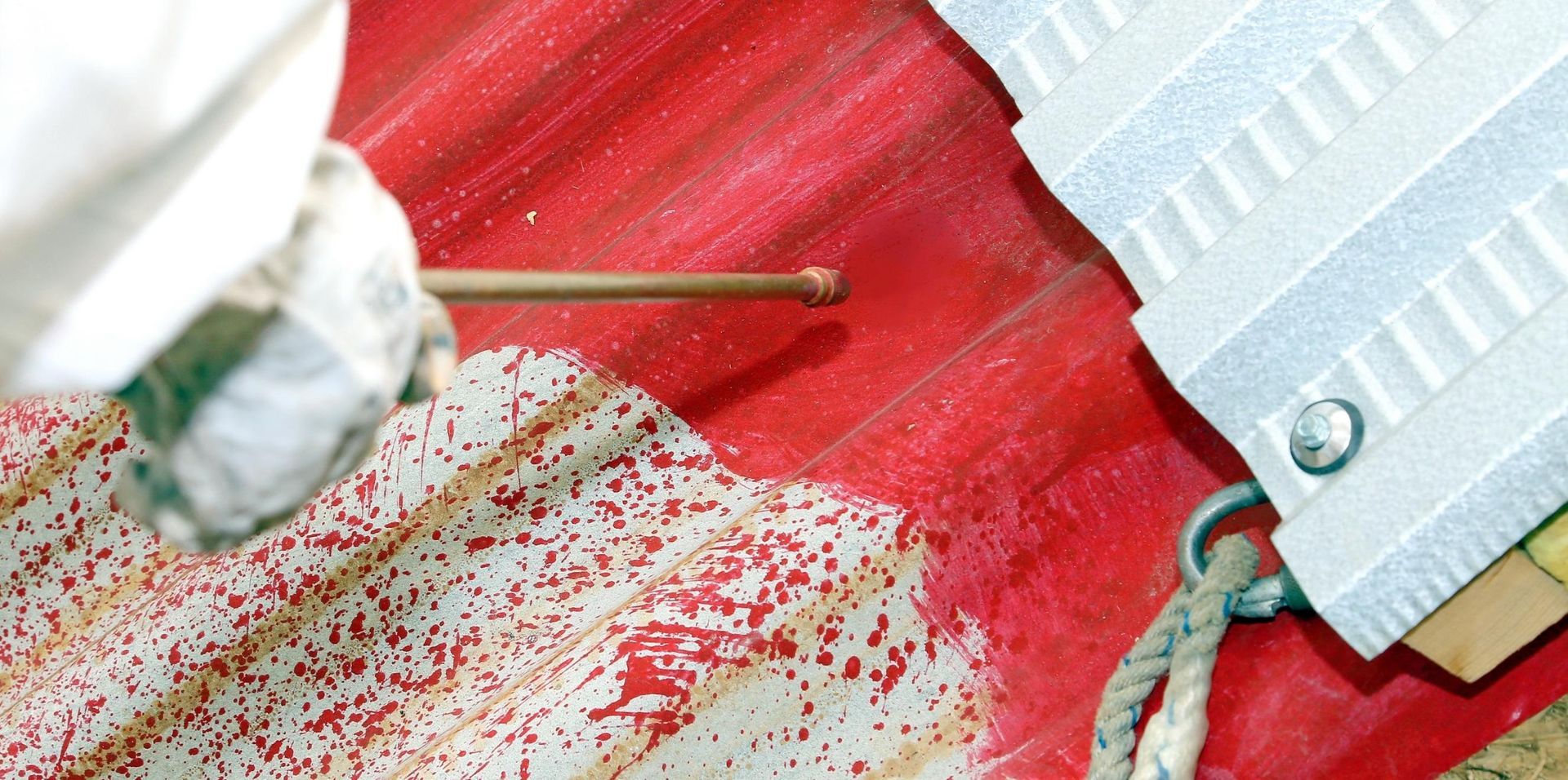 A person is spraying red paint on a red roof.