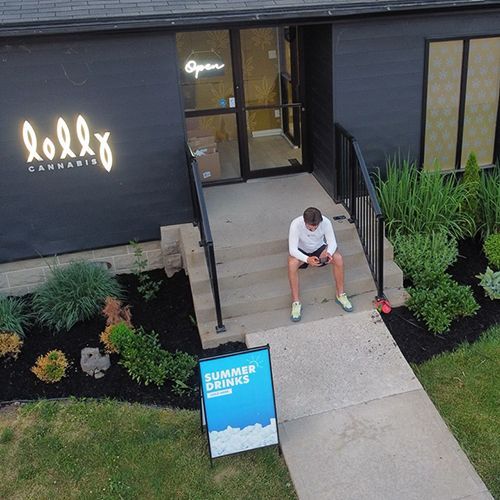 A person sits on the concrete steps of a modern cafe called Lolly, with a blue 