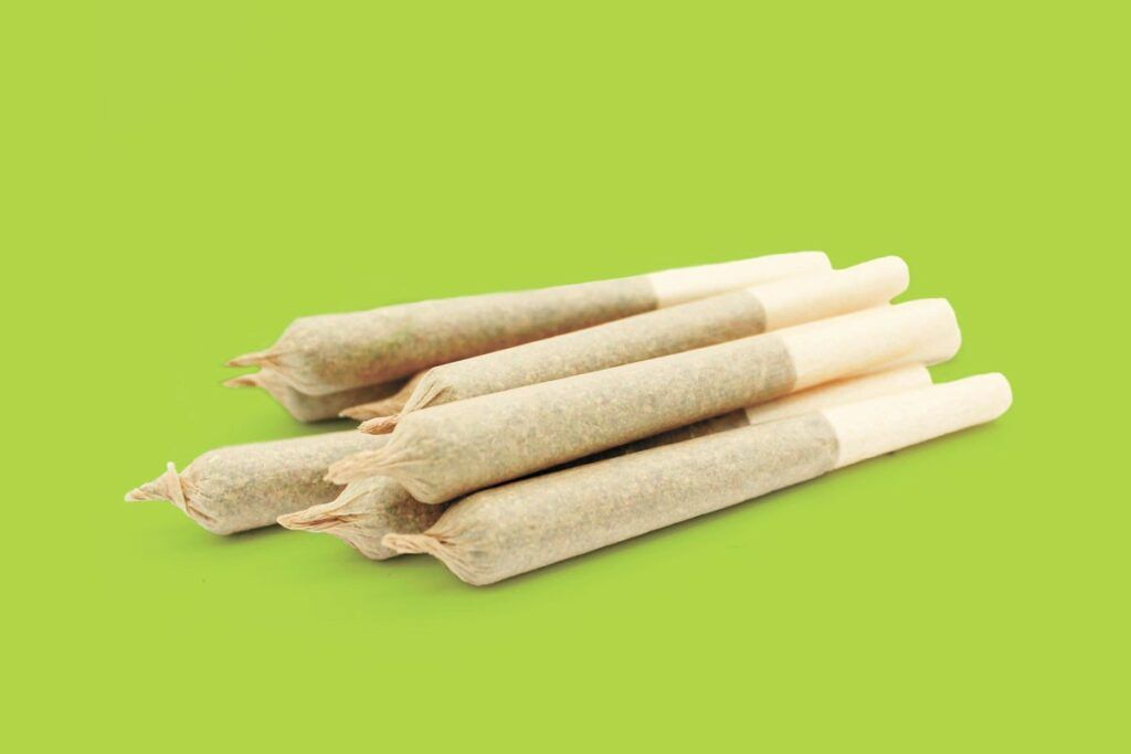 A small pile of hand-rolled pre-roll joints with paper filters against a solid light green background.