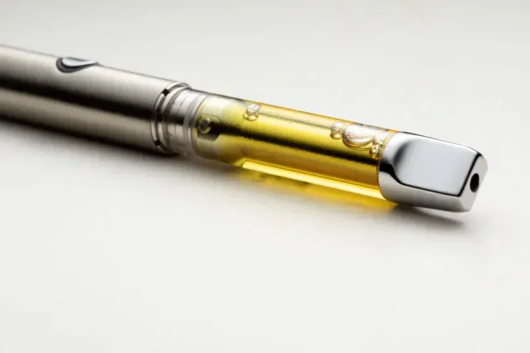 A silver vape pen with a clear cartridge filled with yellow oil, isolated on a white background.
