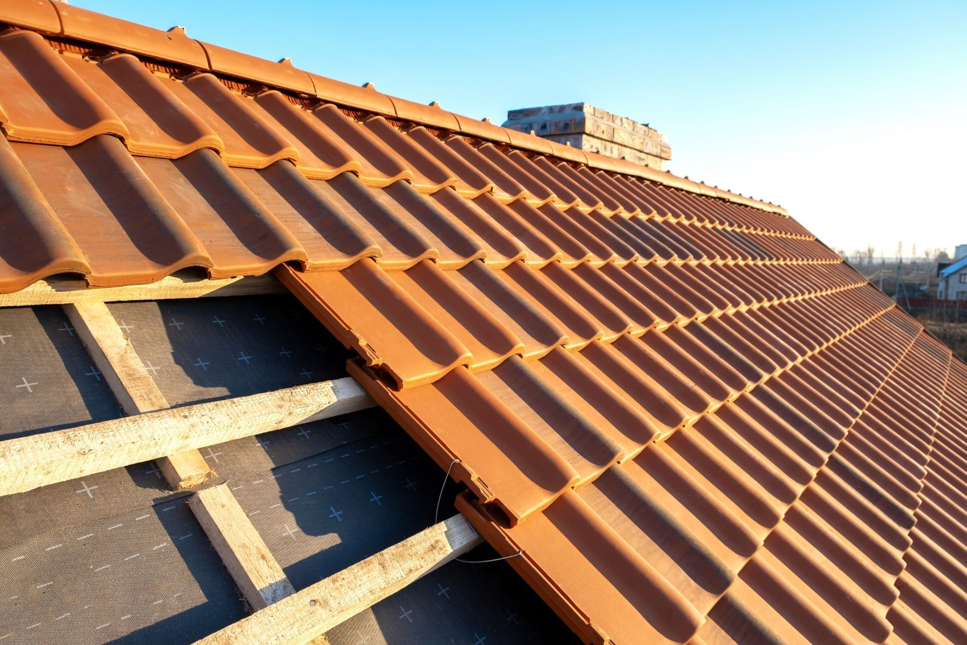 Close-up of a partially tiled roof with terracotta clay tiles installed over wooden battens and black roofing felt.