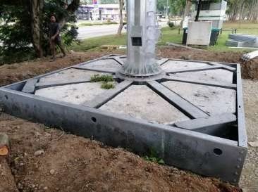 Metal light pole base installed in ground, with concrete fill and support beams.