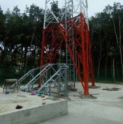 Red and white telecommunications tower under construction, set in a forest area.