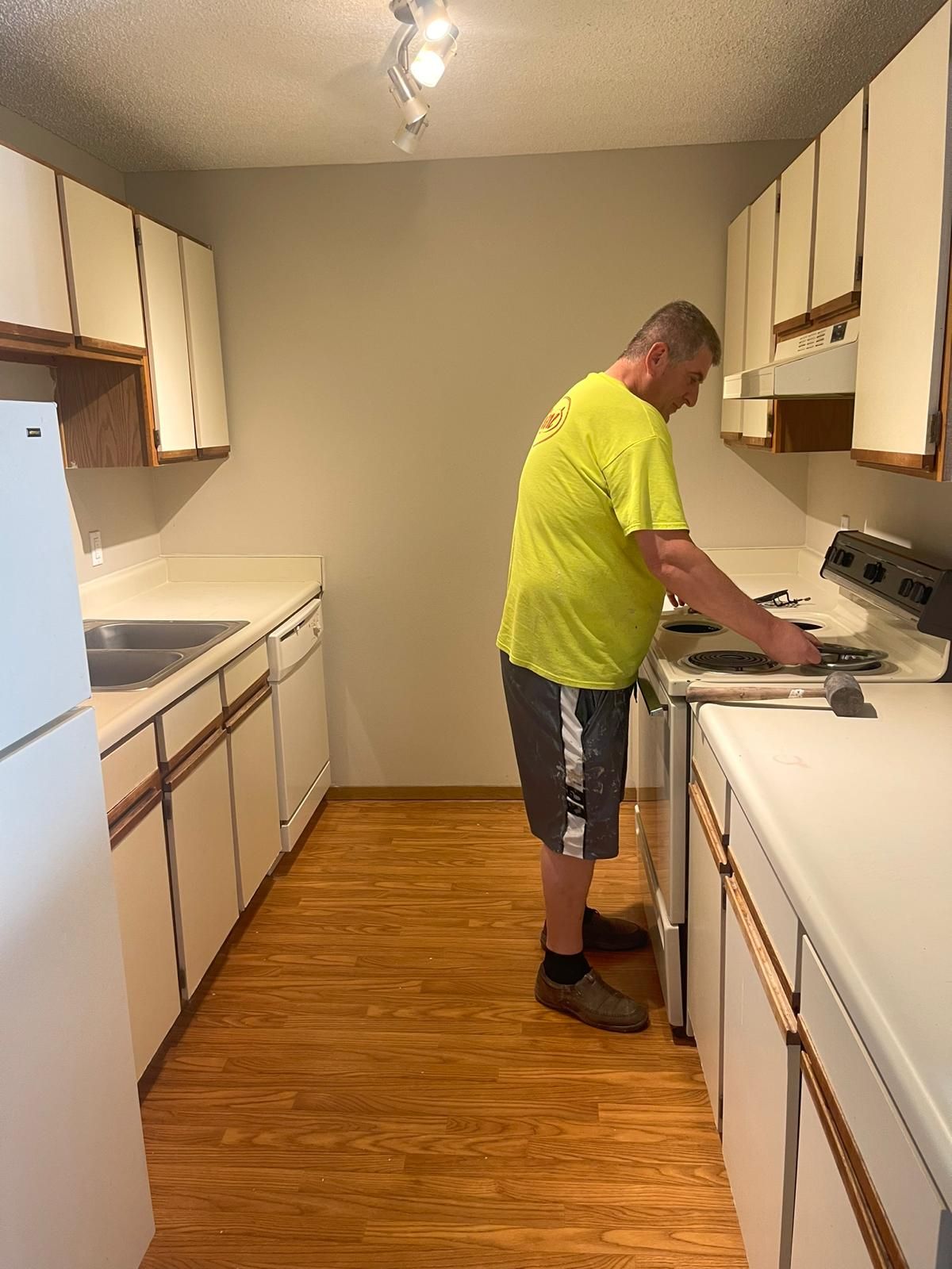 A man in a yellow shirt is working on a stove in a kitchen.