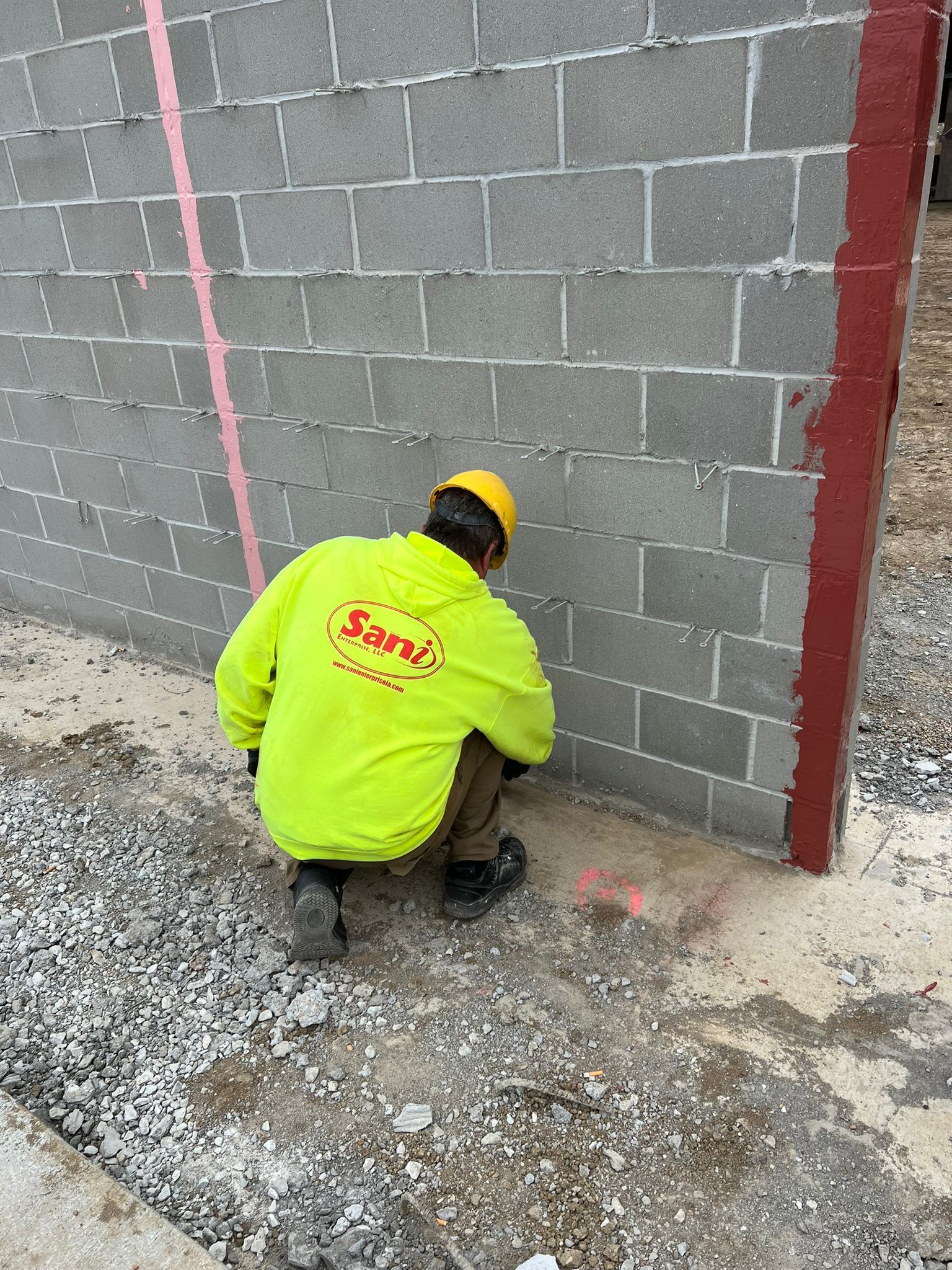 A man in a neon yellow jacket is kneeling down next to a brick wall.