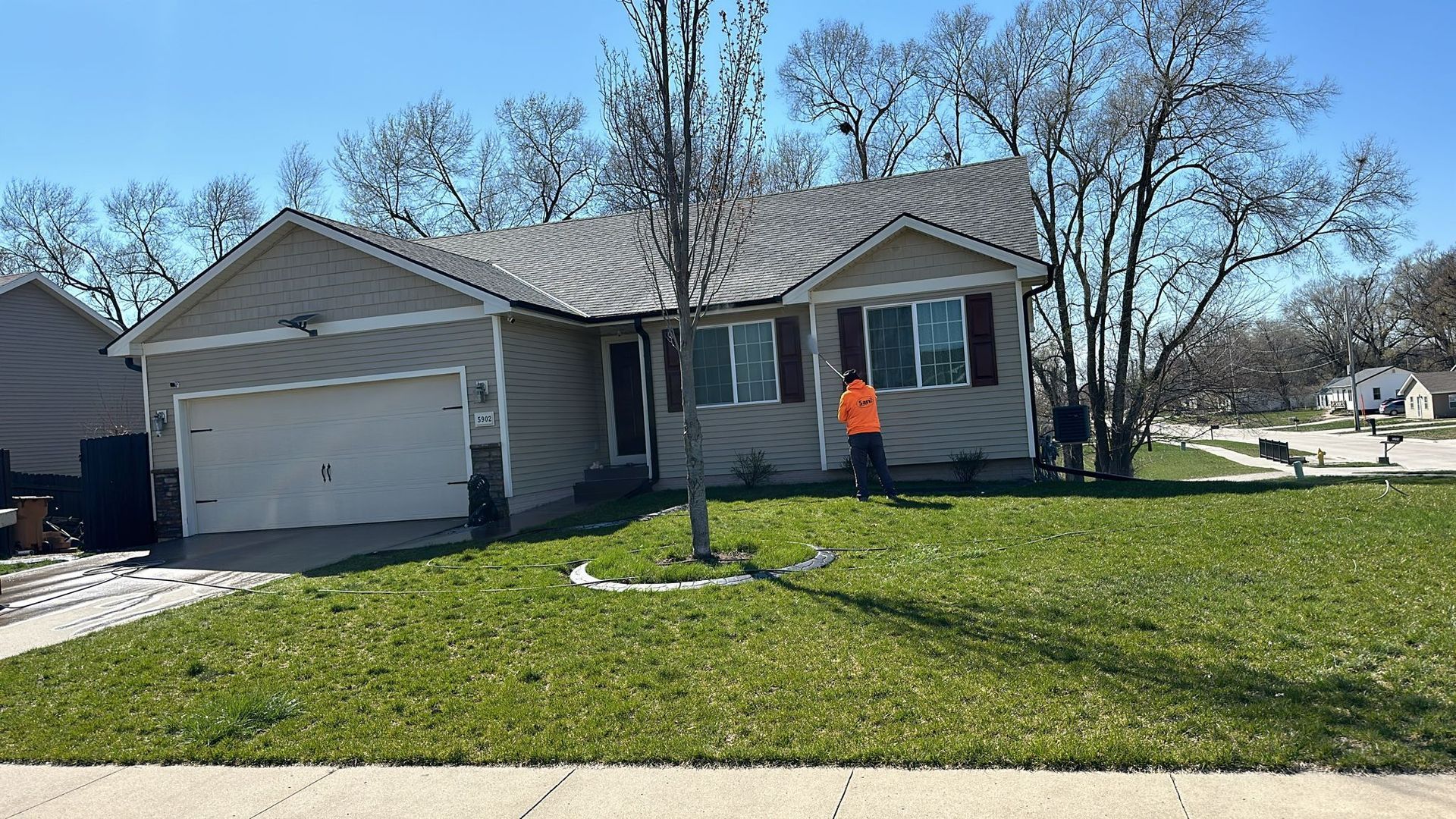 A man in an orange shirt is standing in front of a house.