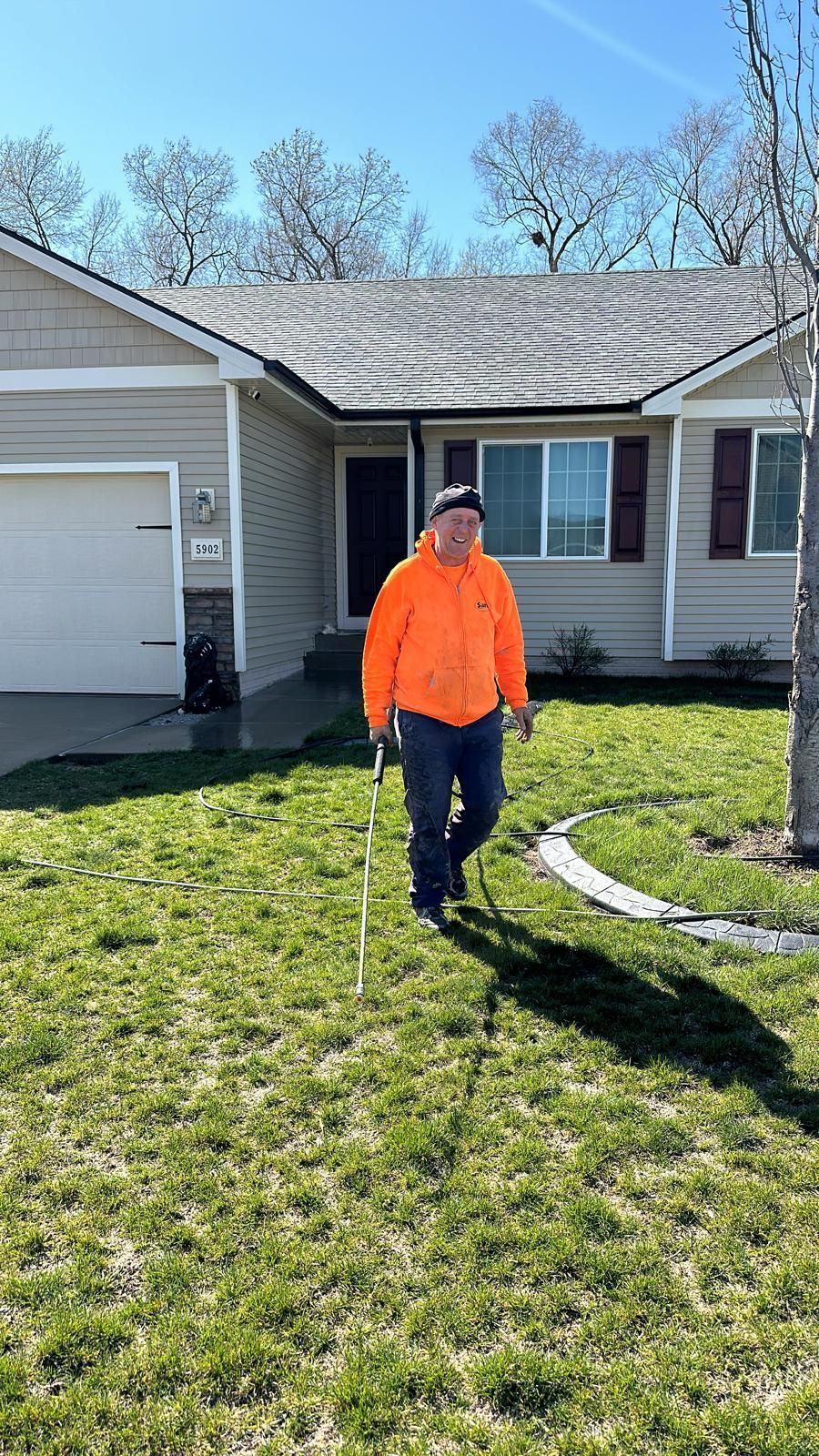 A man in an orange jacket is standing in front of a house.