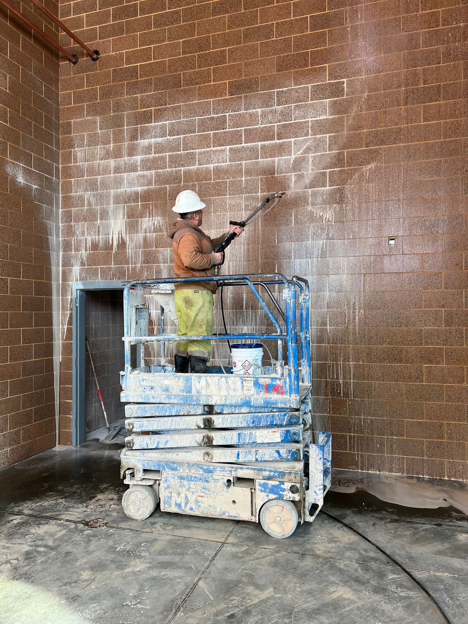 A man is cleaning a brick wall on a scissor lift.