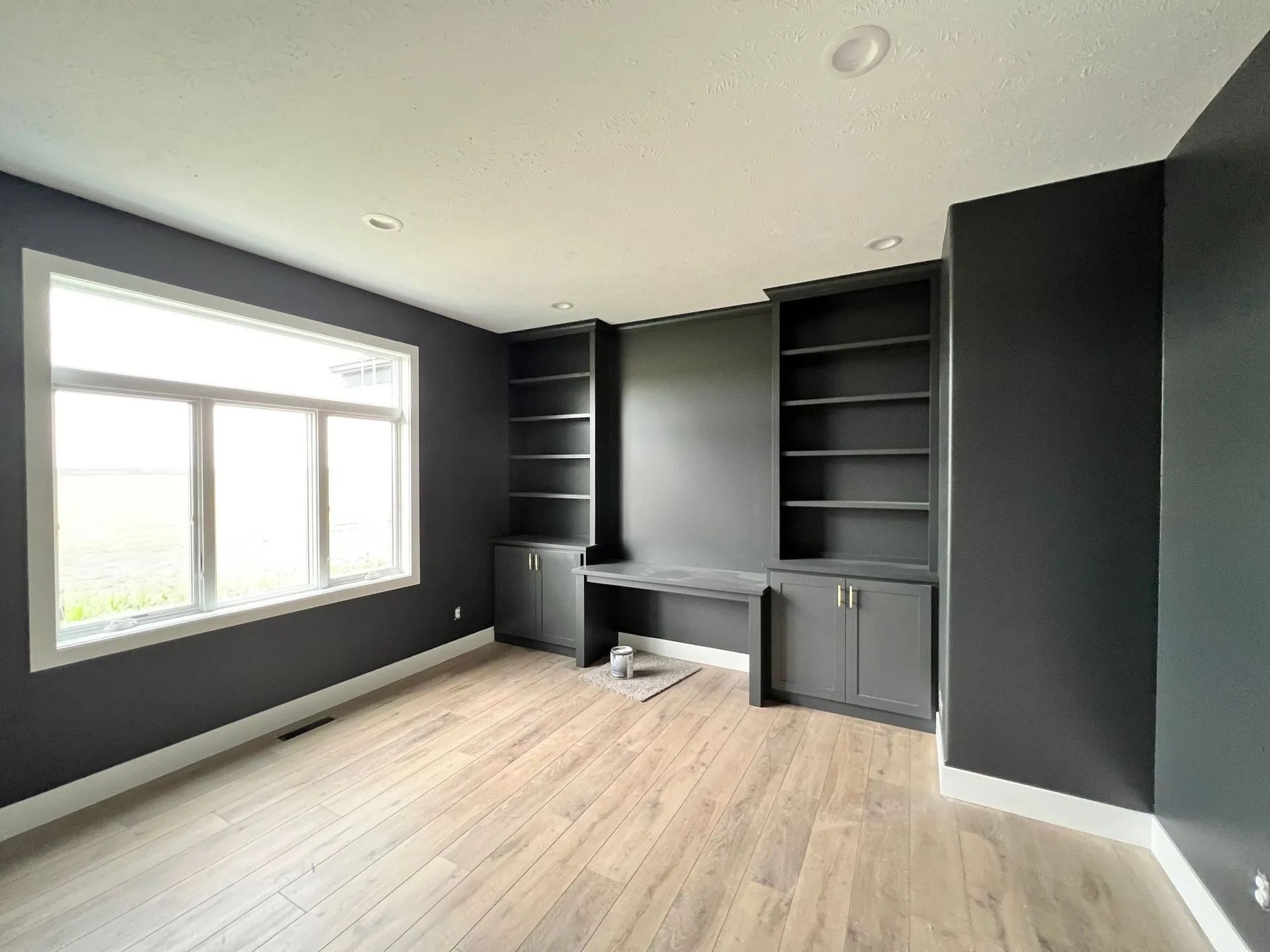 An empty room with a desk , shelves , and a window.