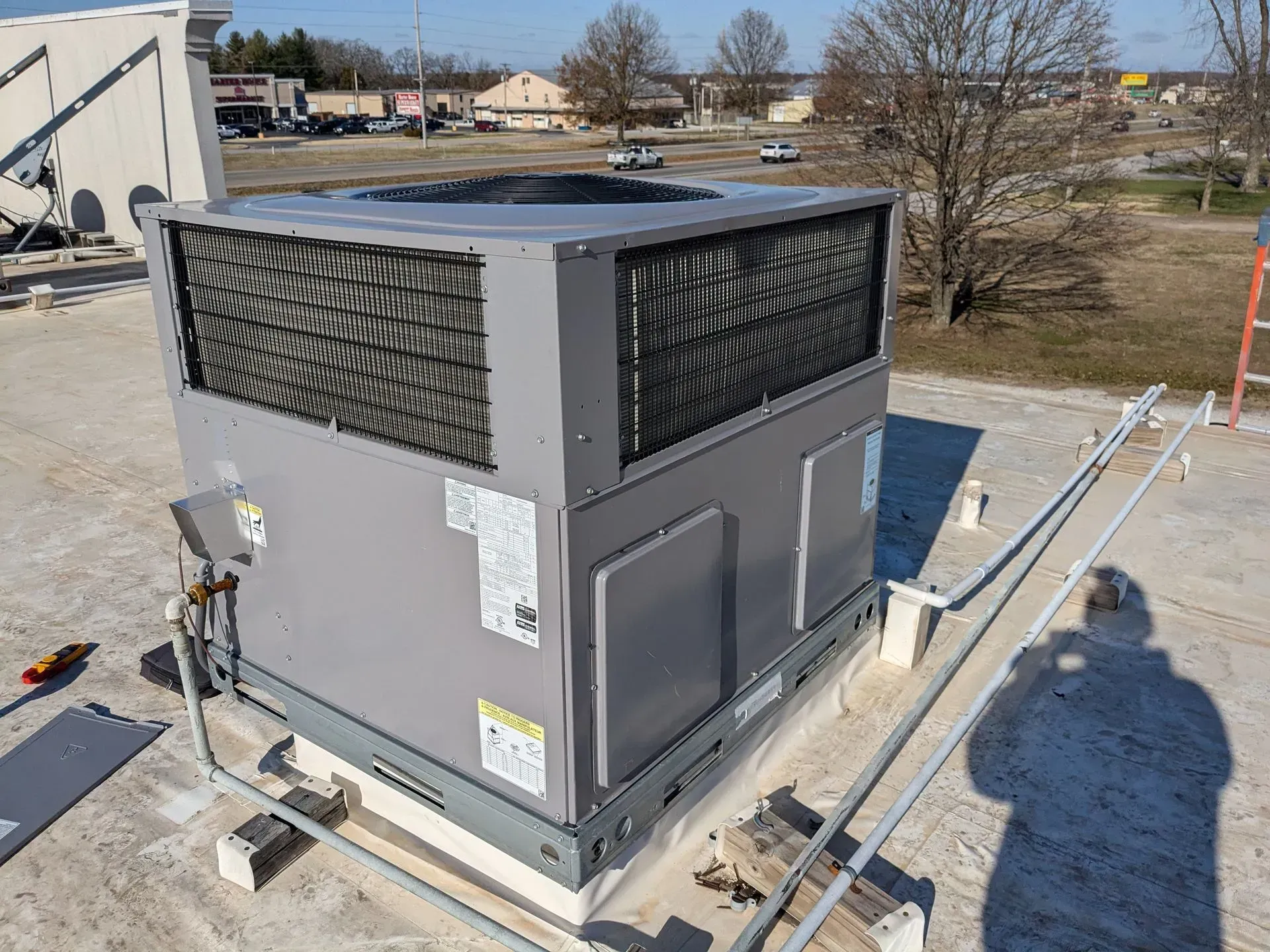Rooftop HVAC unit, gray with black grilles, on a flat roof with pipes and other equipment.