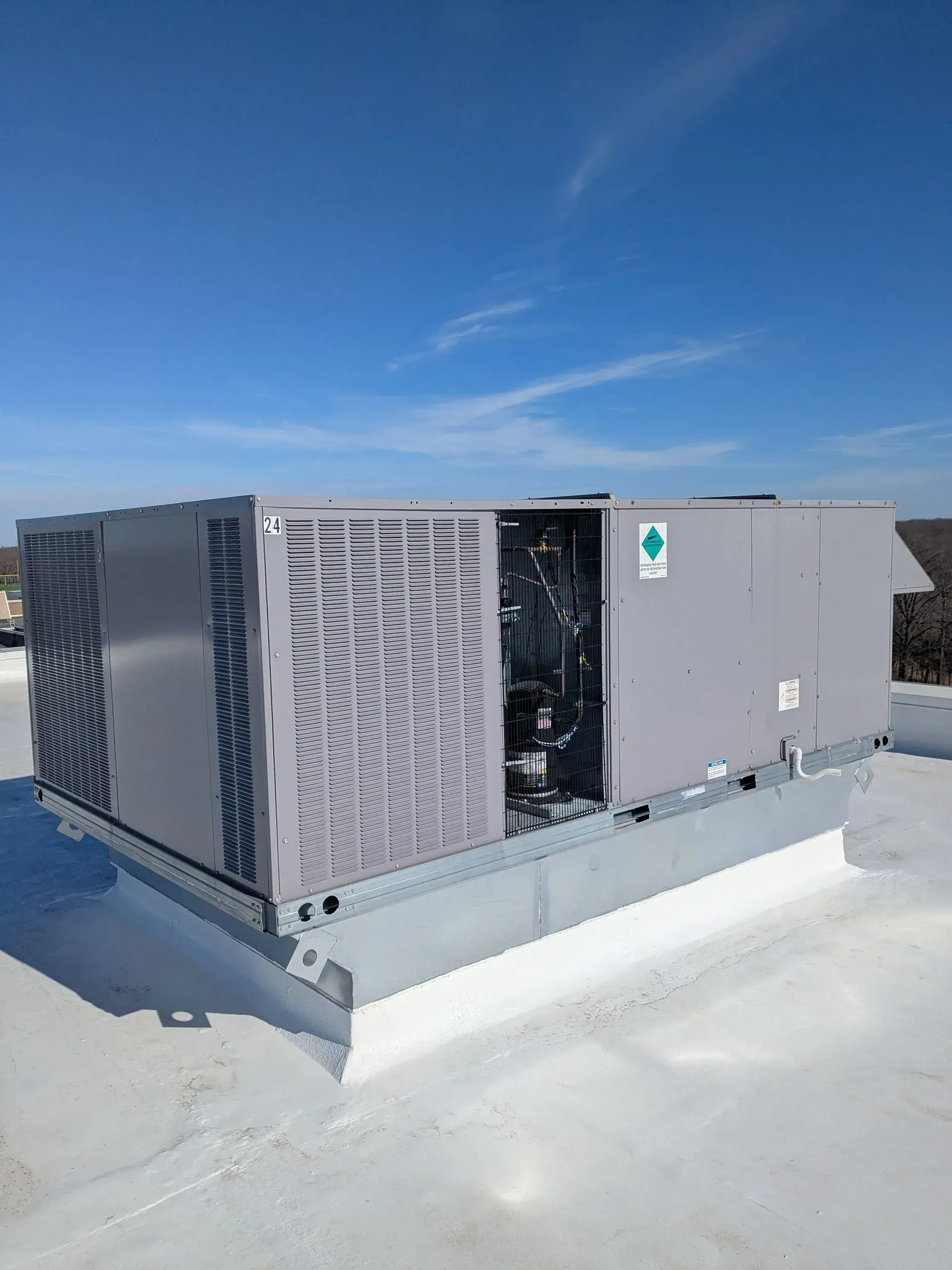 Rooftop HVAC unit on a white roof under a blue sky. Gray unit, metal supports.