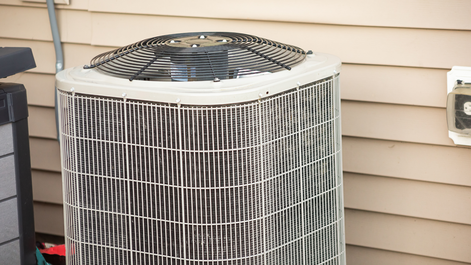 Rooftop HVAC unit, gray with black grilles, on a flat roof with pipes and other equipment.